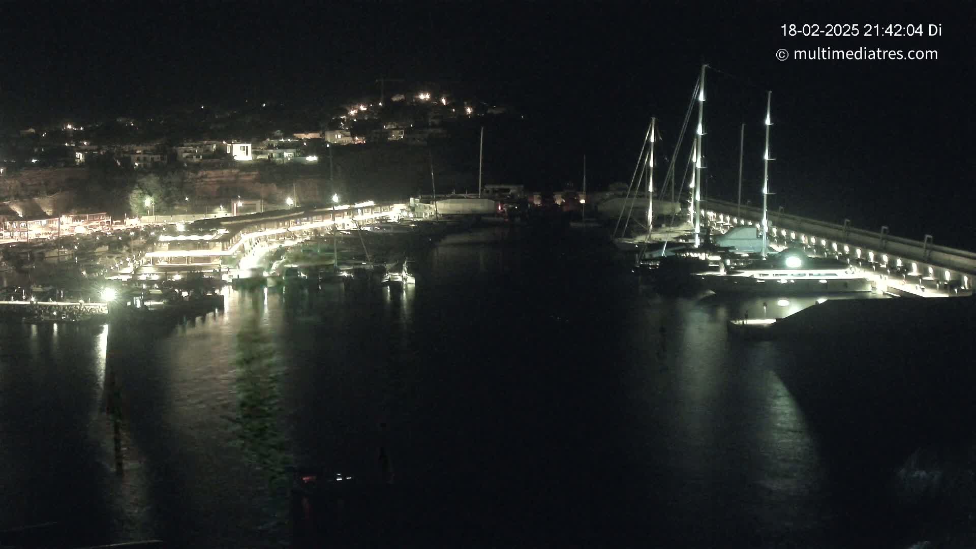 A nighttime view of a marina filled with boats, lit up against a dark hillside.