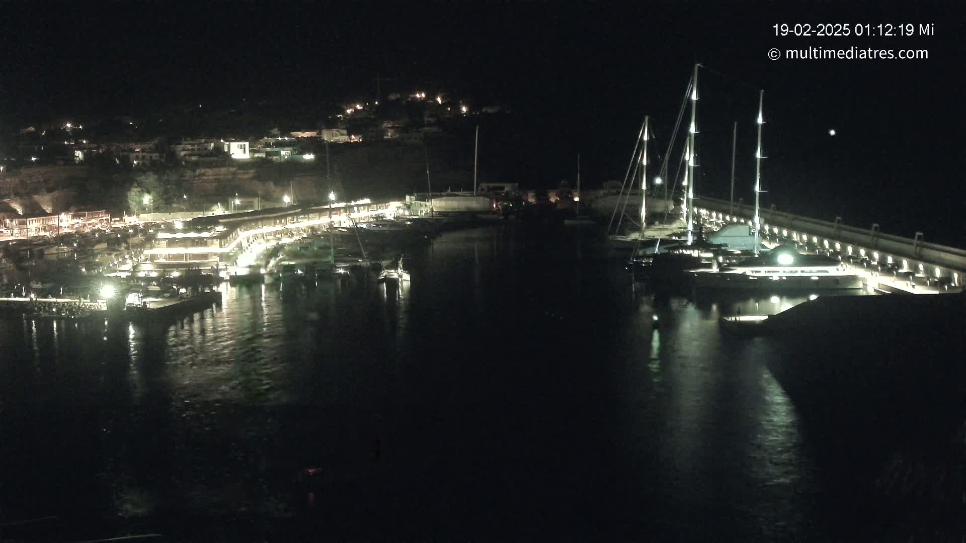 A nighttime view of a marina filled with boats, illuminated buildings, and calm water.