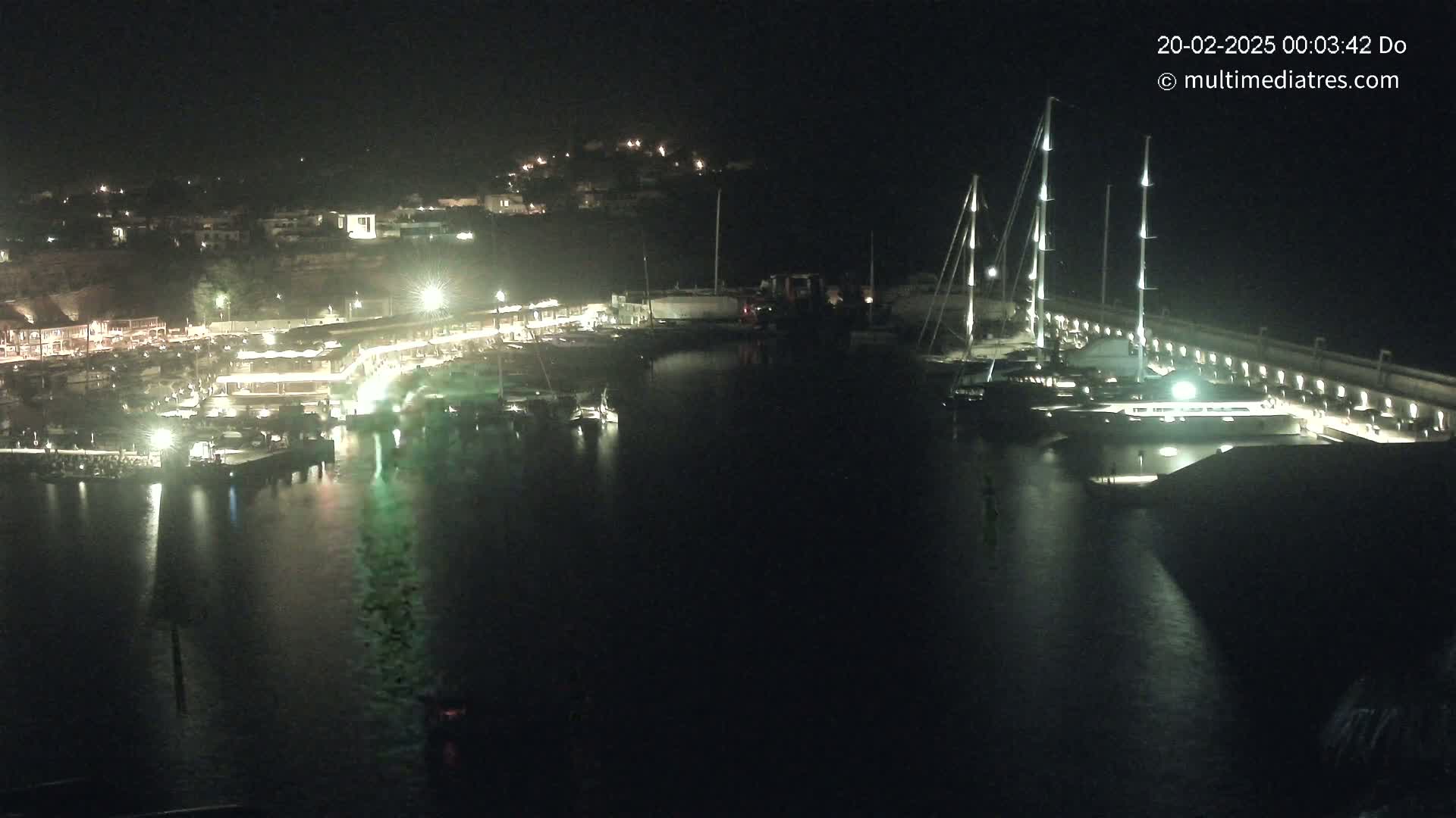 A nighttime view of a harbor filled with boats, illuminated by lights along the docks and buildings on the shore.