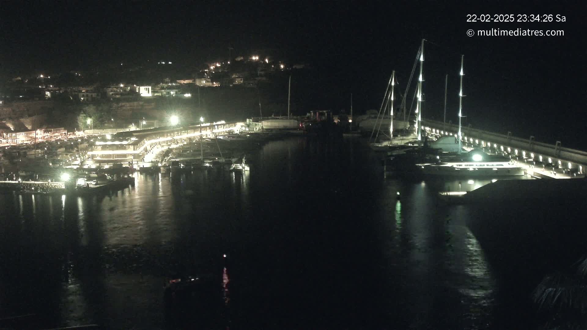 A nighttime view of a harbor filled with boats, illuminated by lights on the docks and buildings along the shore.