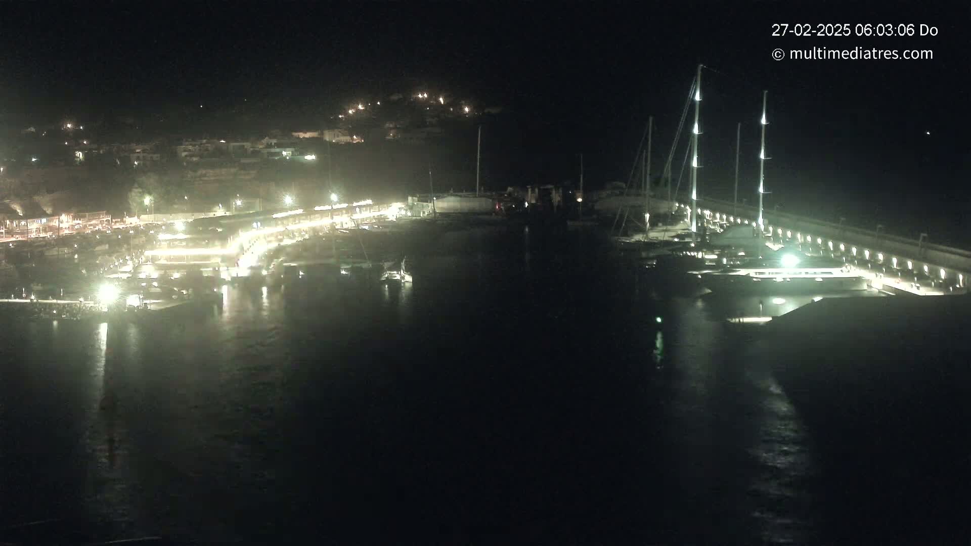 A nighttime view of a harbor filled with boats, lit up by lights along the docks and buildings on the shore.