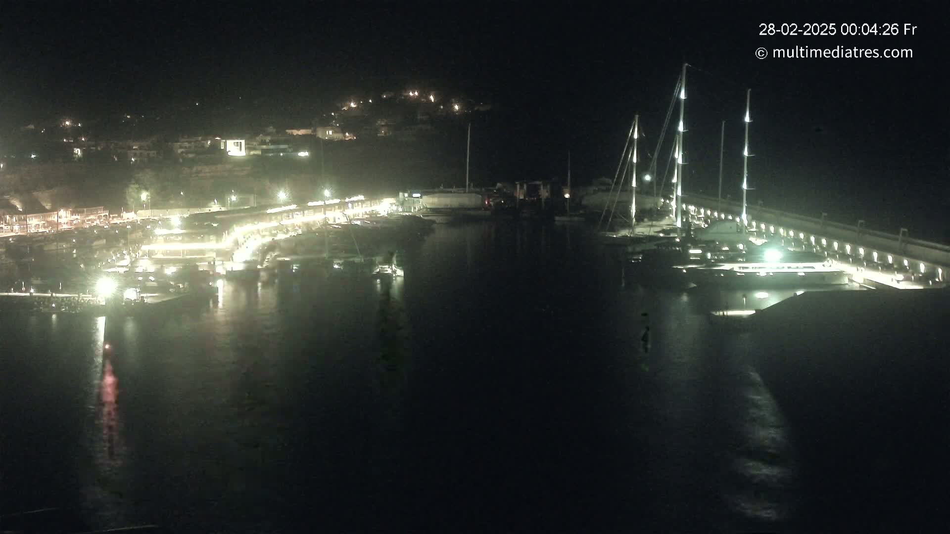 A nighttime aerial view of a marina, with numerous boats docked and lights illuminating the waterfront.
