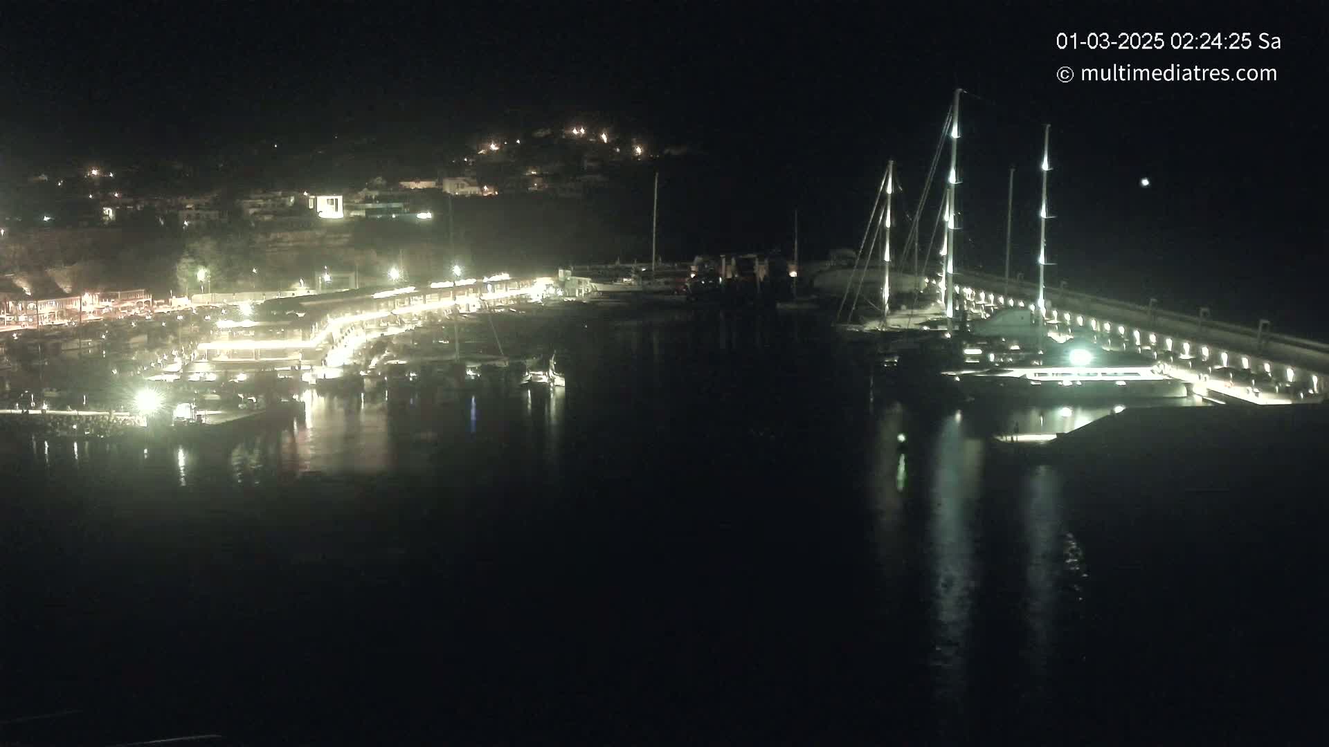 A nighttime view of a marina with docked boats and illuminated buildings along the waterfront.