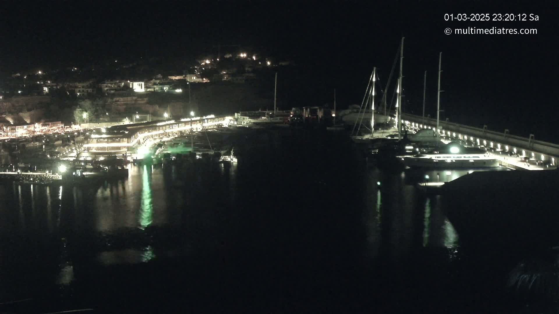 A nighttime view of a marina filled with boats, illuminated buildings, and calm water.