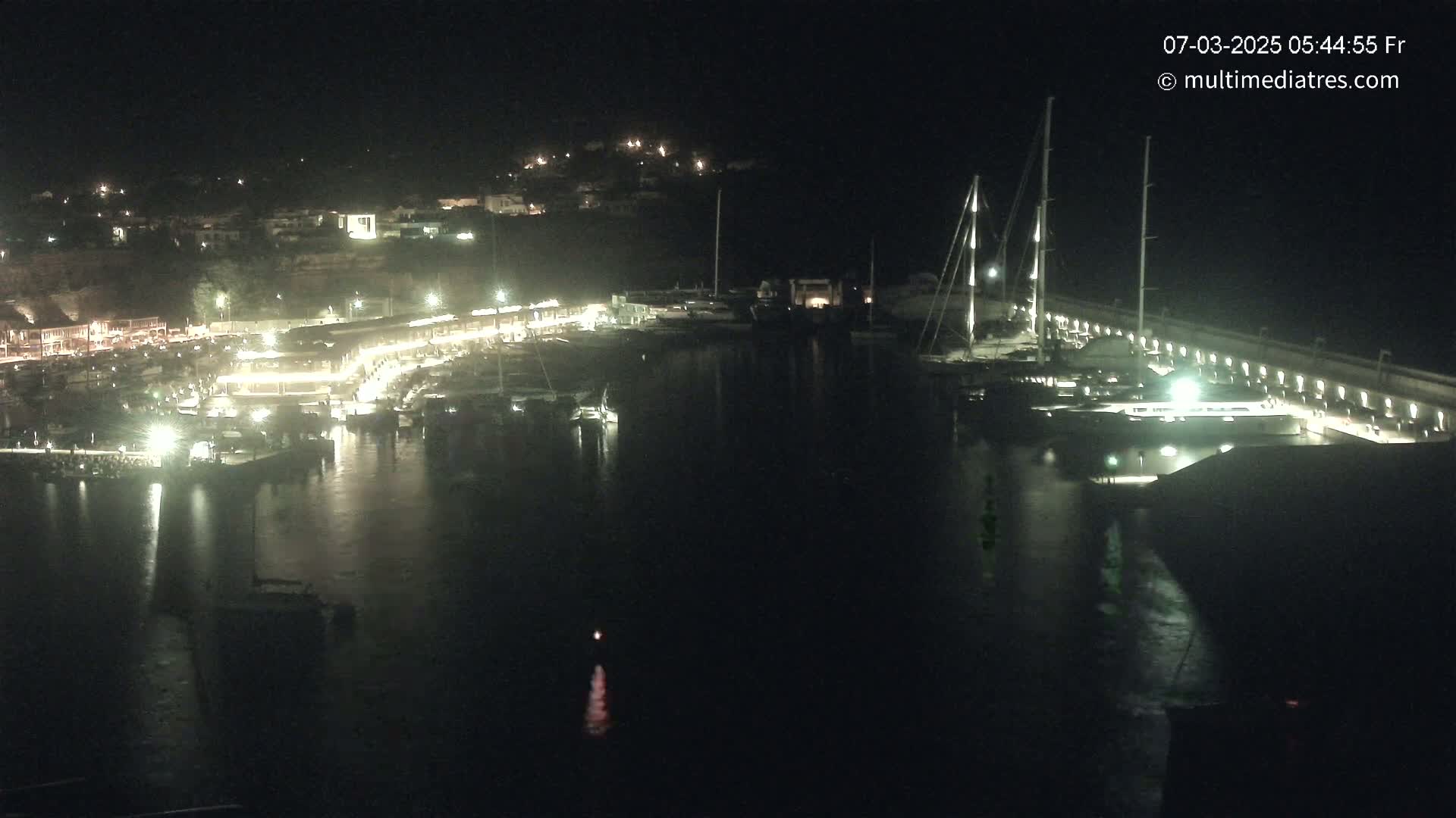 A nighttime view of a harbor filled with boats and lit buildings along the waterfront.