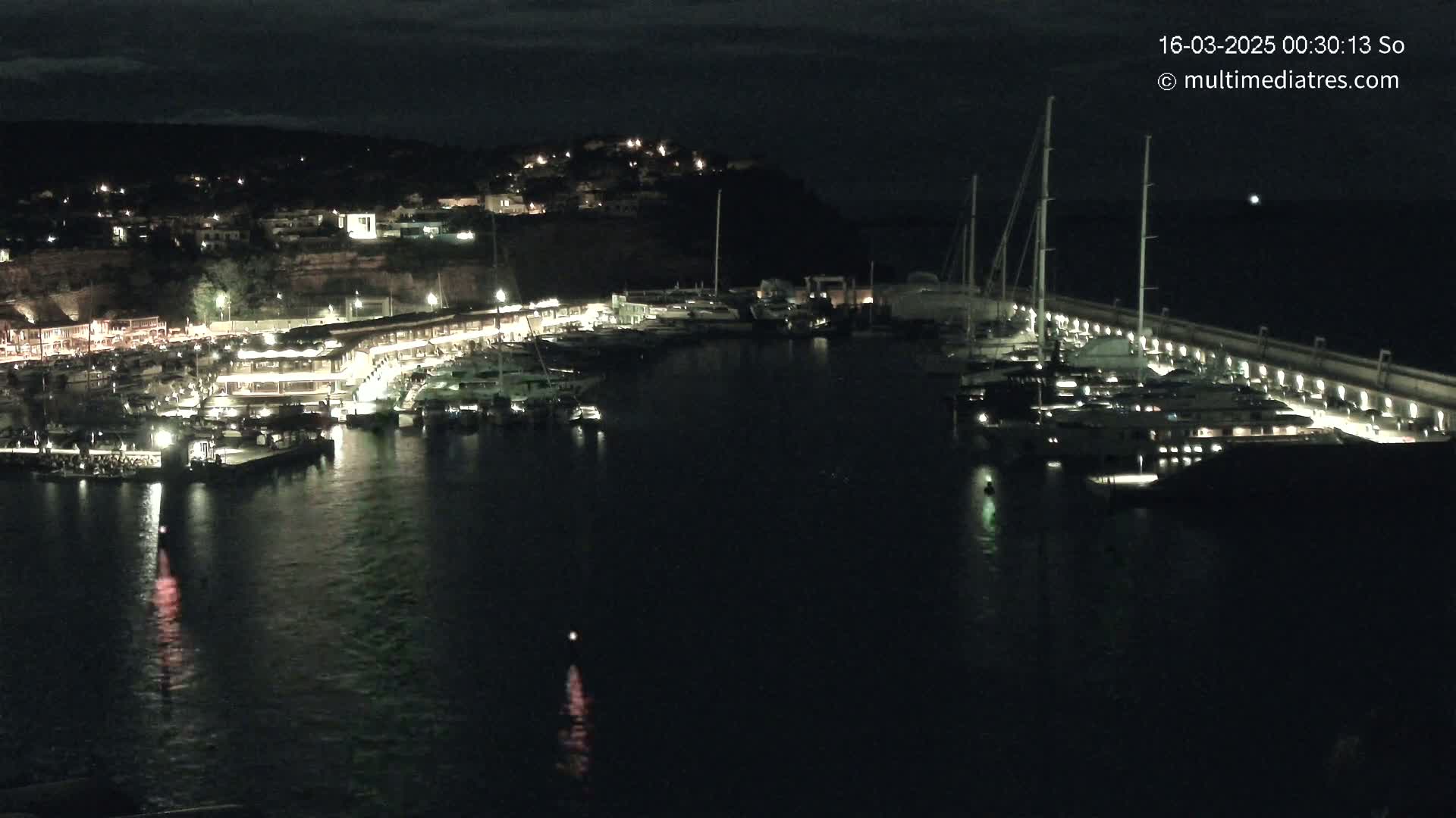 A marina filled with yachts and boats is illuminated at night, under a dark sky.