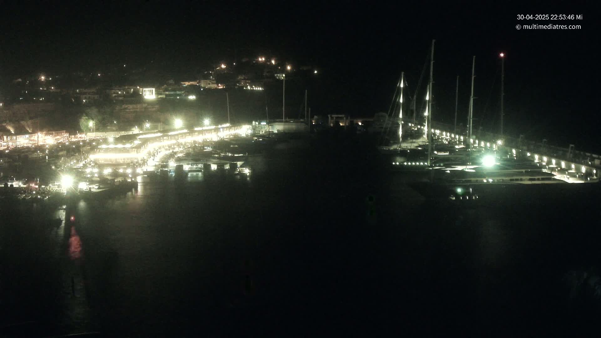 A nighttime, aerial view of a marina filled with boats, illuminated by lights along the docks and buildings on the shore.