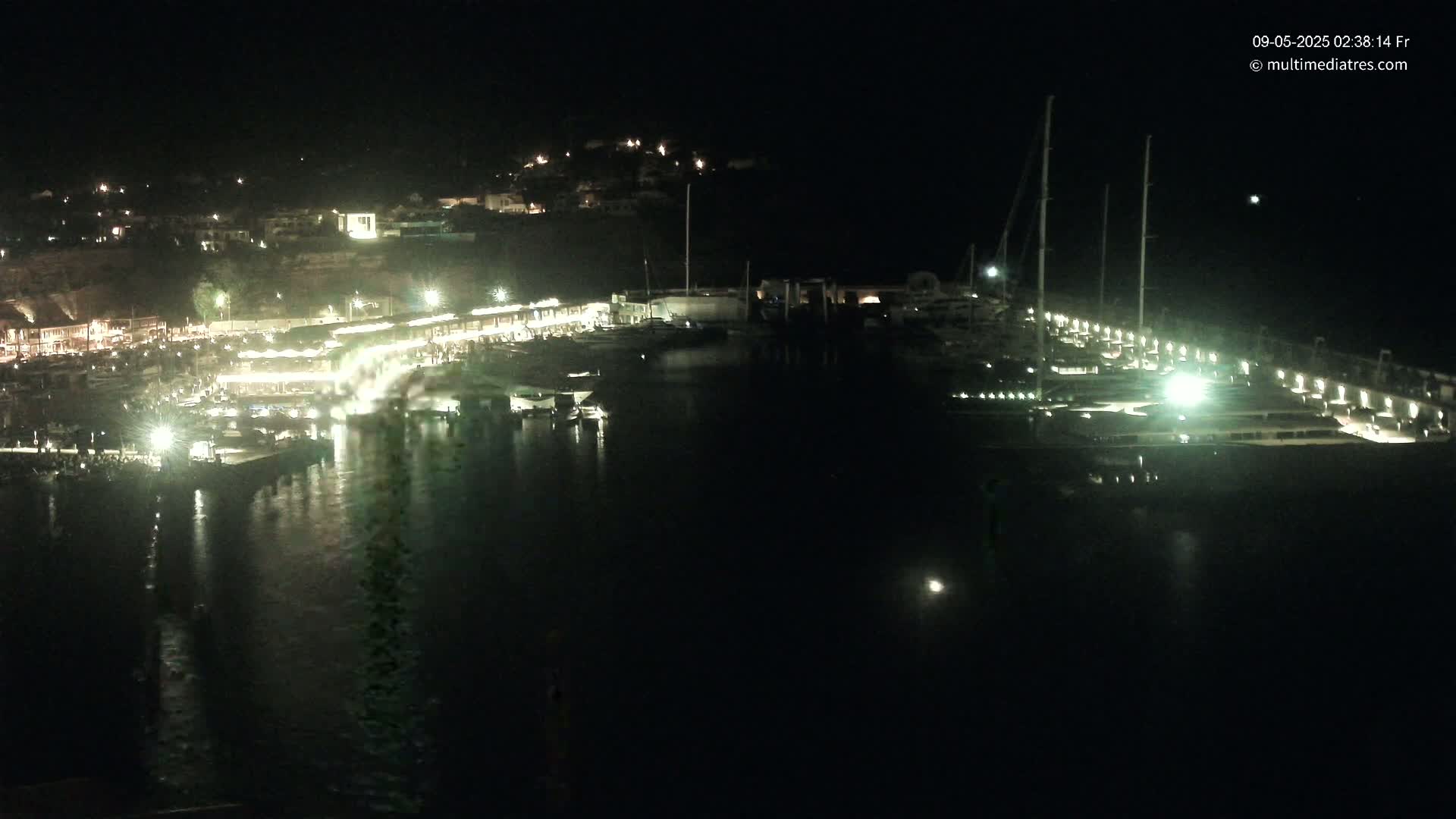 A nighttime view of a harbor filled with boats, illuminated by lights along the docks and buildings on the shore.