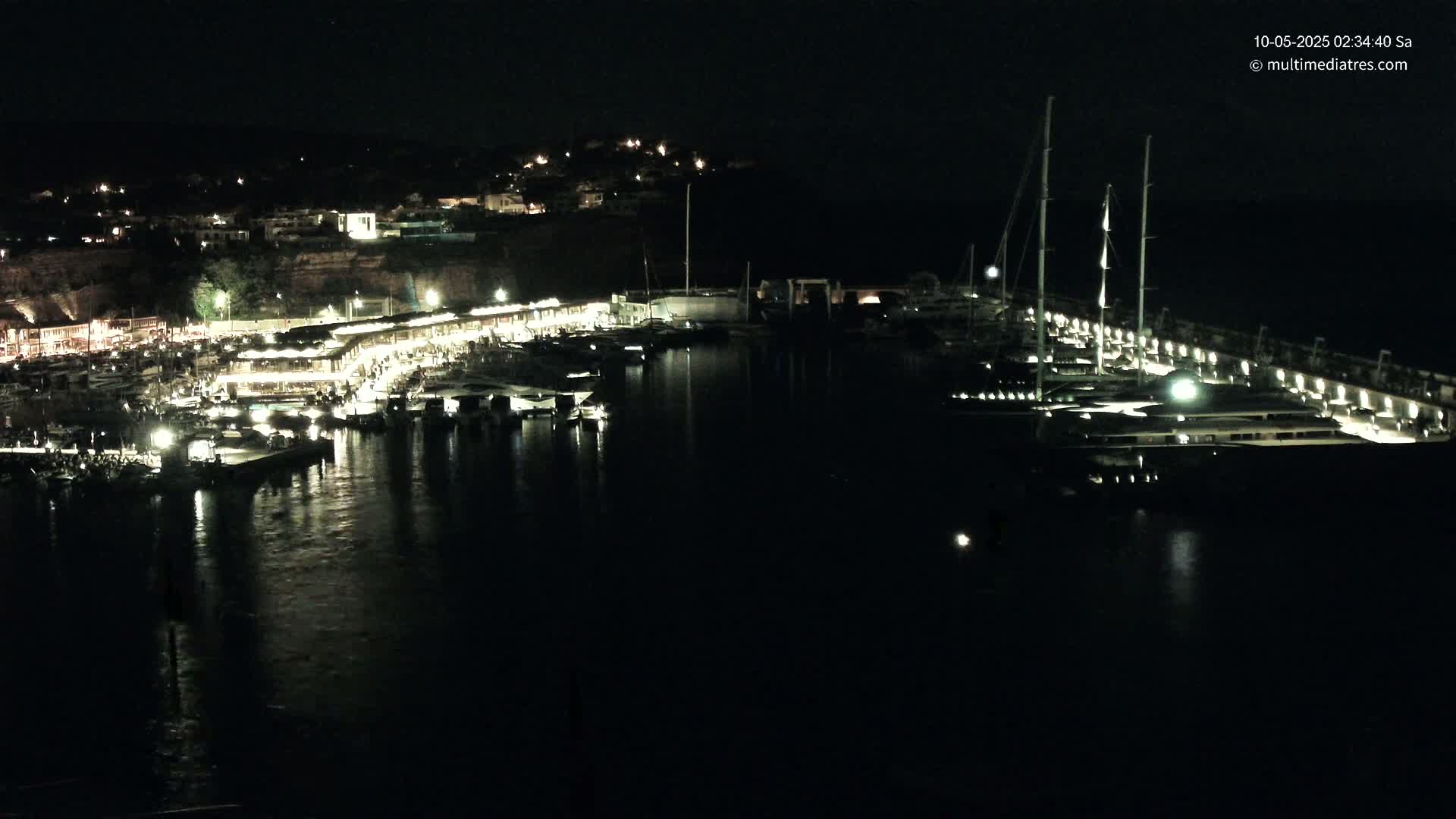 A nighttime view of a harbor filled with boats and a town illuminated on a hill overlooking the water.