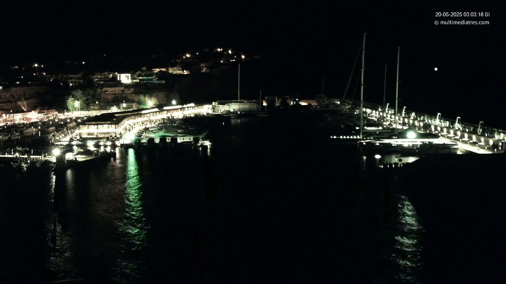 A nighttime view of a harbor filled with boats and illuminated buildings along a dark, calm body of water.