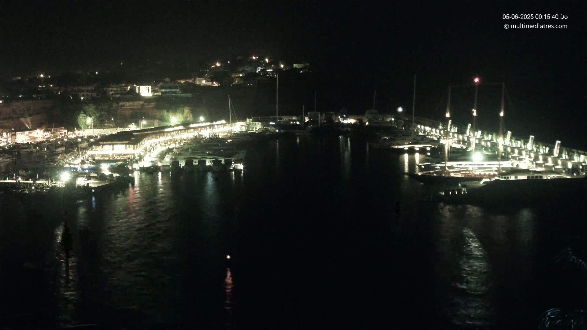 A nighttime view of a harbor filled with boats and lit buildings, on a calm night.