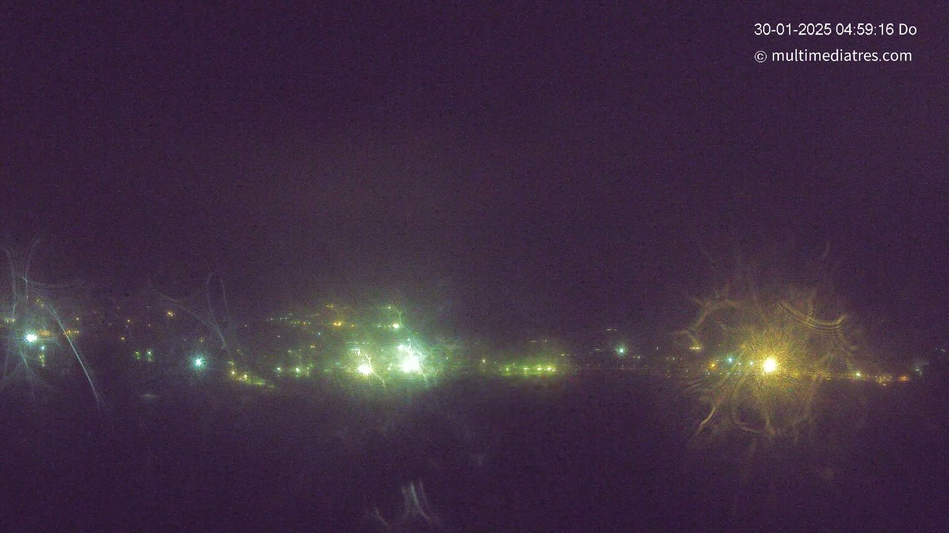 A nighttime long shot shows a distant town with scattered lights under a dark, clear sky.