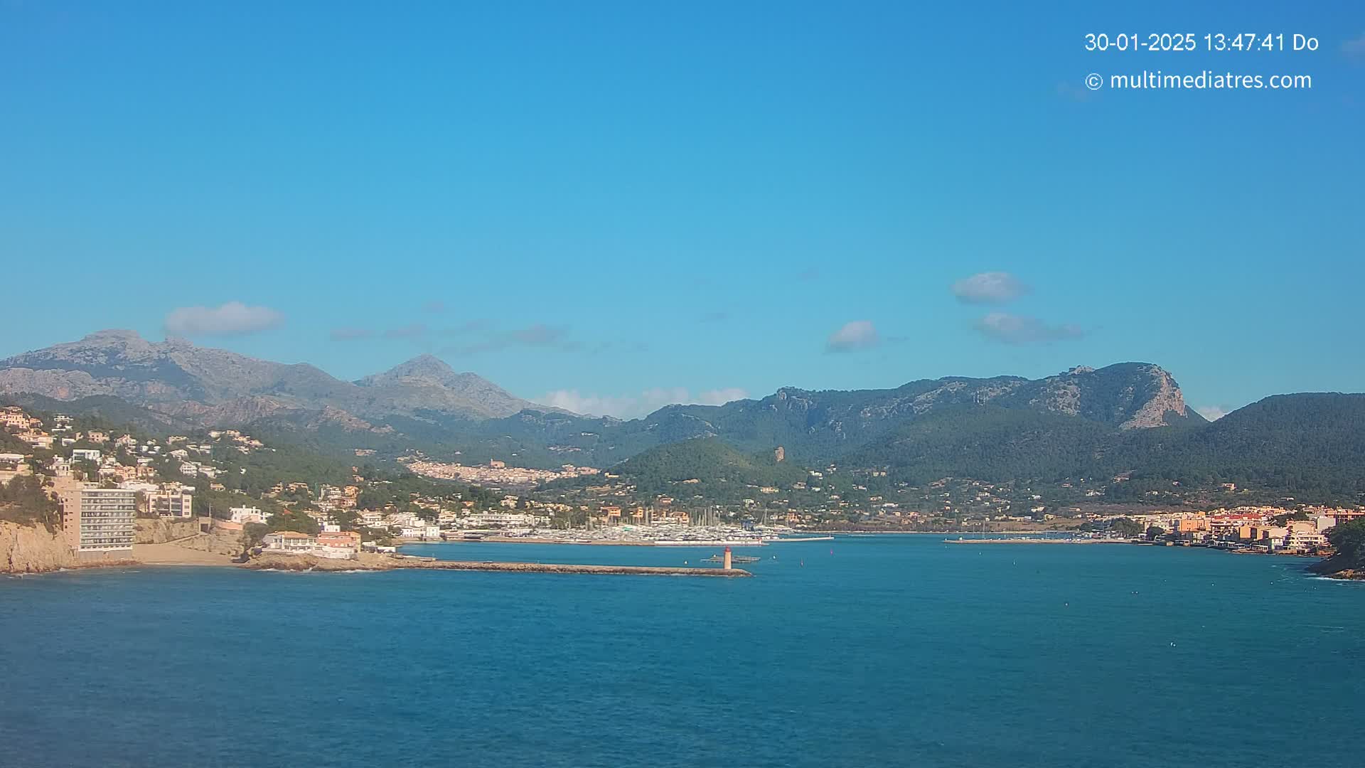 A coastal town nestled between mountains and a calm, blue sea under a clear, sunny sky.