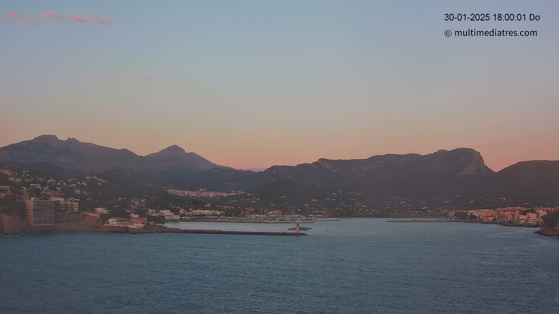 A coastal town nestled between mountains, with a calm harbor and a soft pink sunset sky.