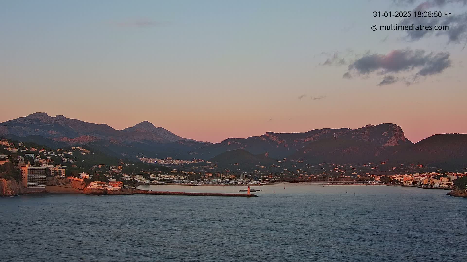 A coastal town nestled between mountains at sunset, with calm waters in the foreground.