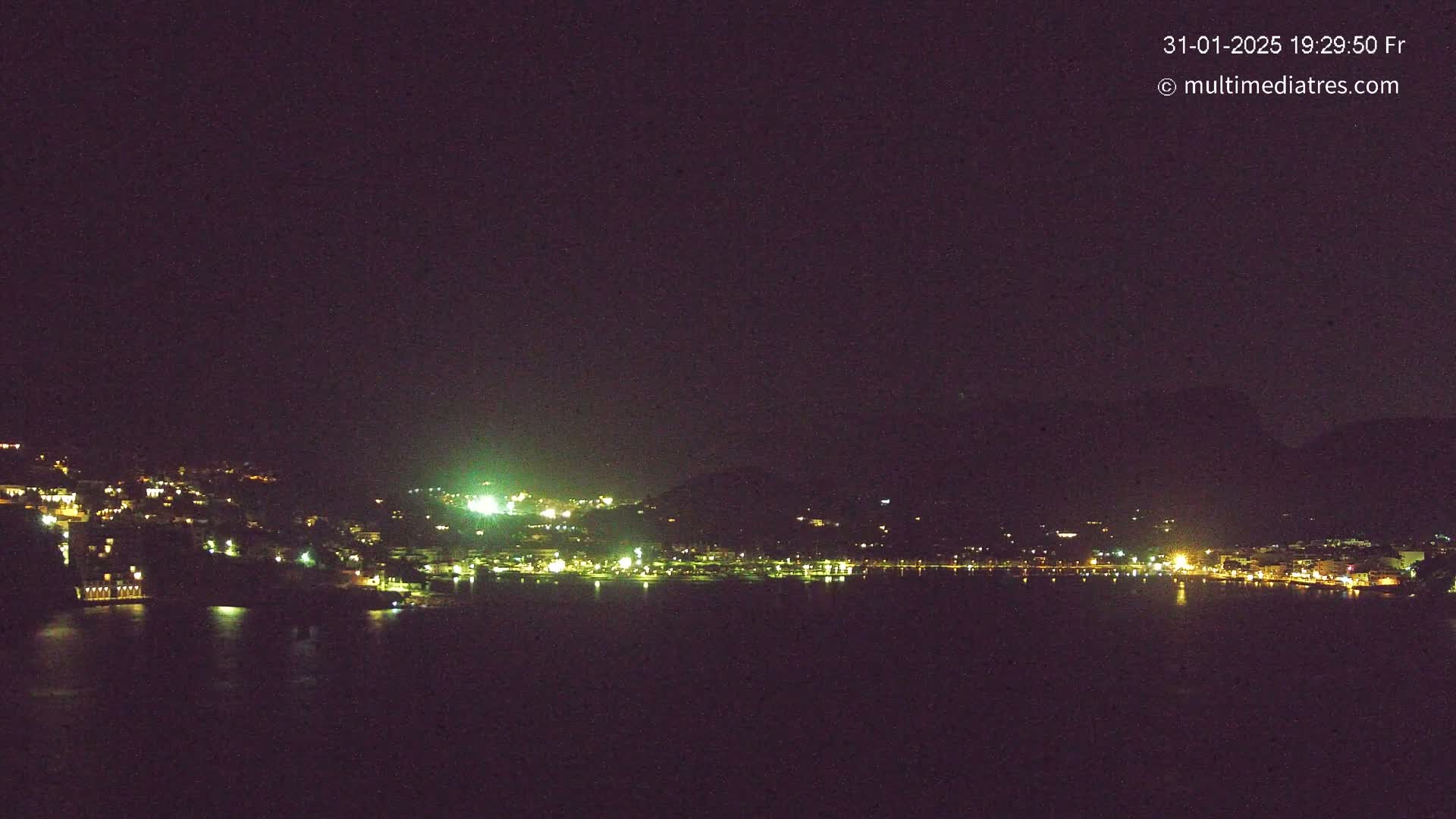 A nighttime view of a coastal town with its lights reflecting on dark water under a clear sky.
