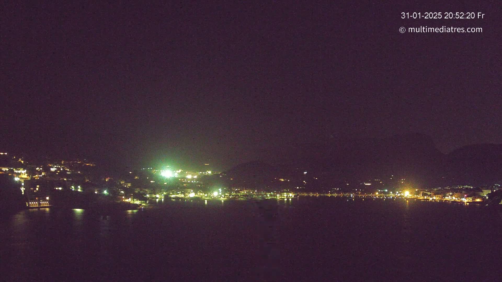 A nighttime view of a town's lights illuminated across a dark body of water under a clear, dark sky.