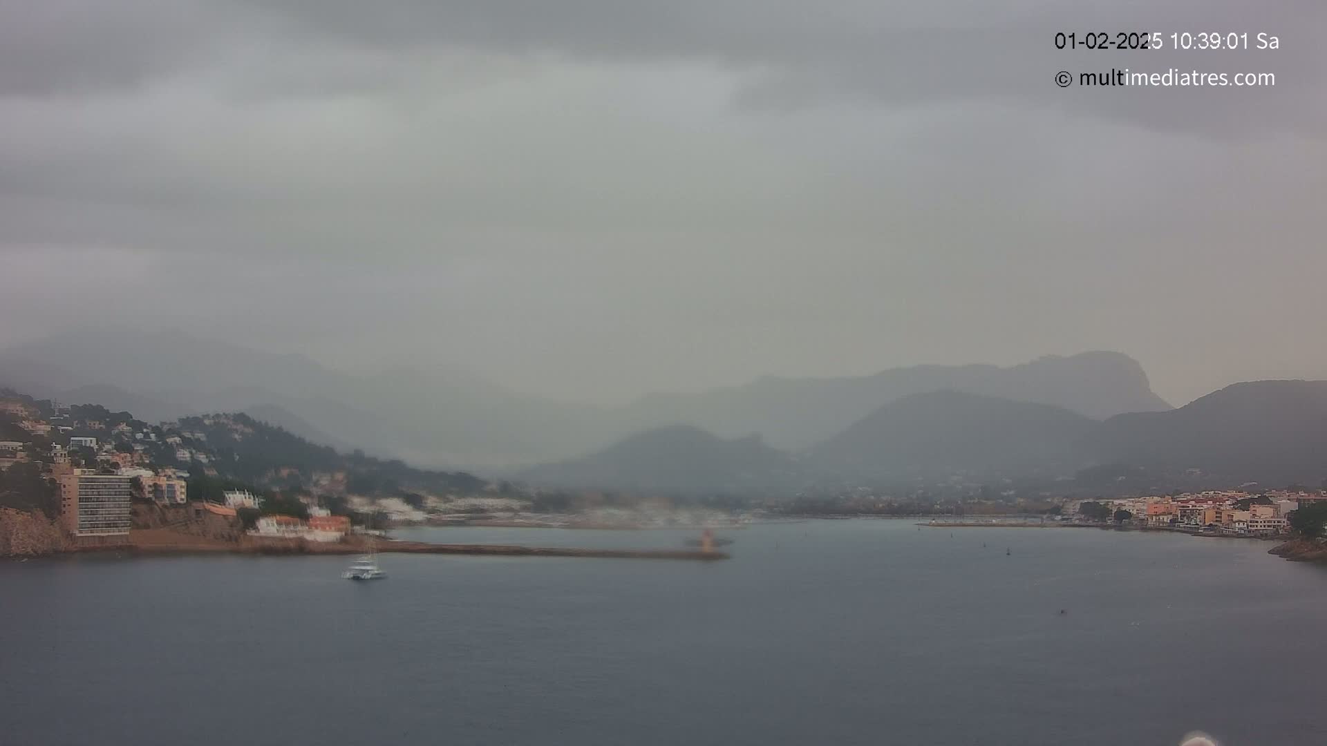 A hazy, overcast day reveals a coastal town nestled between mountains and a calm bay.