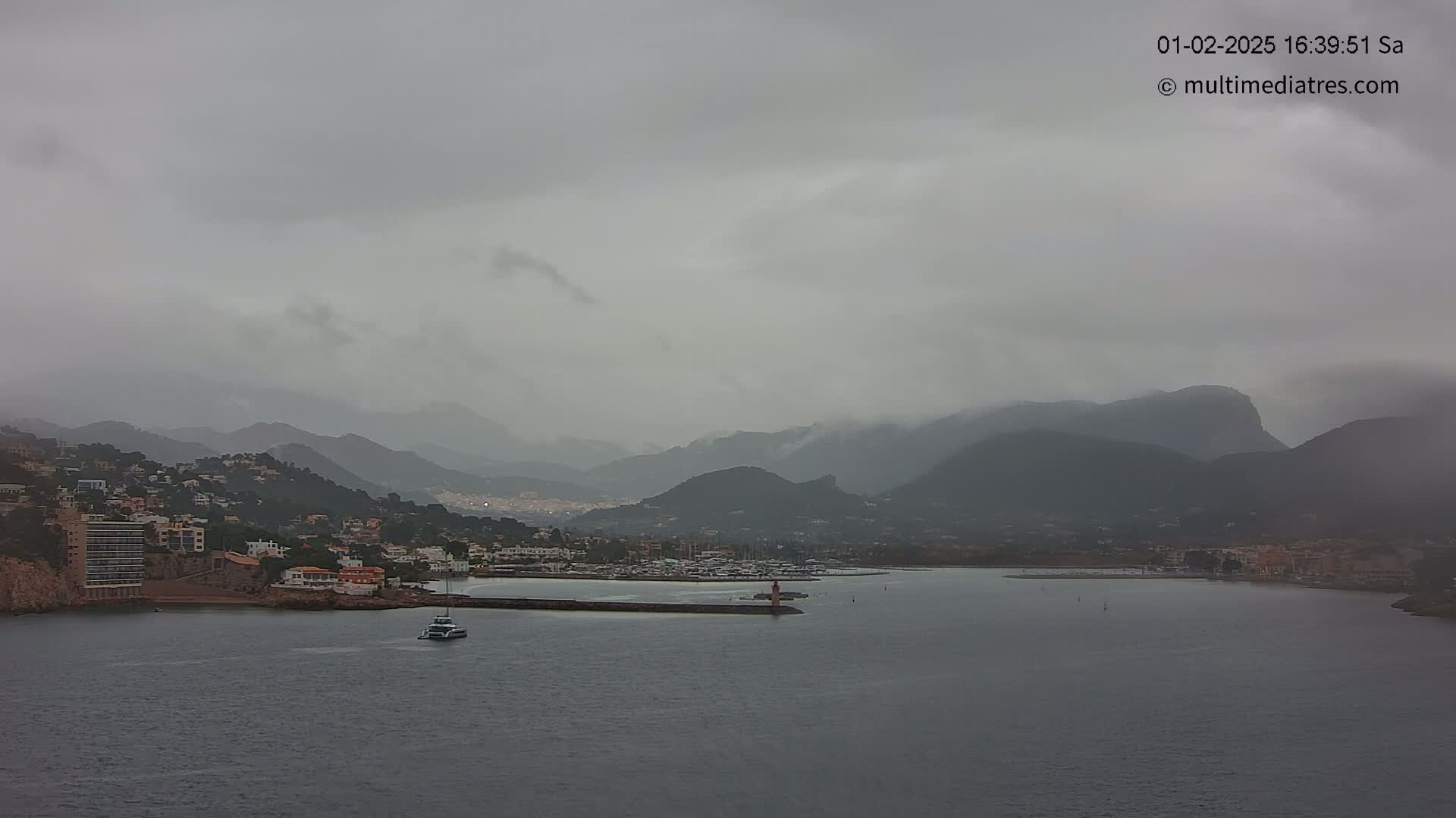 A coastal town nestled between mountains is shrouded in a hazy, overcast sky under a grey sky.