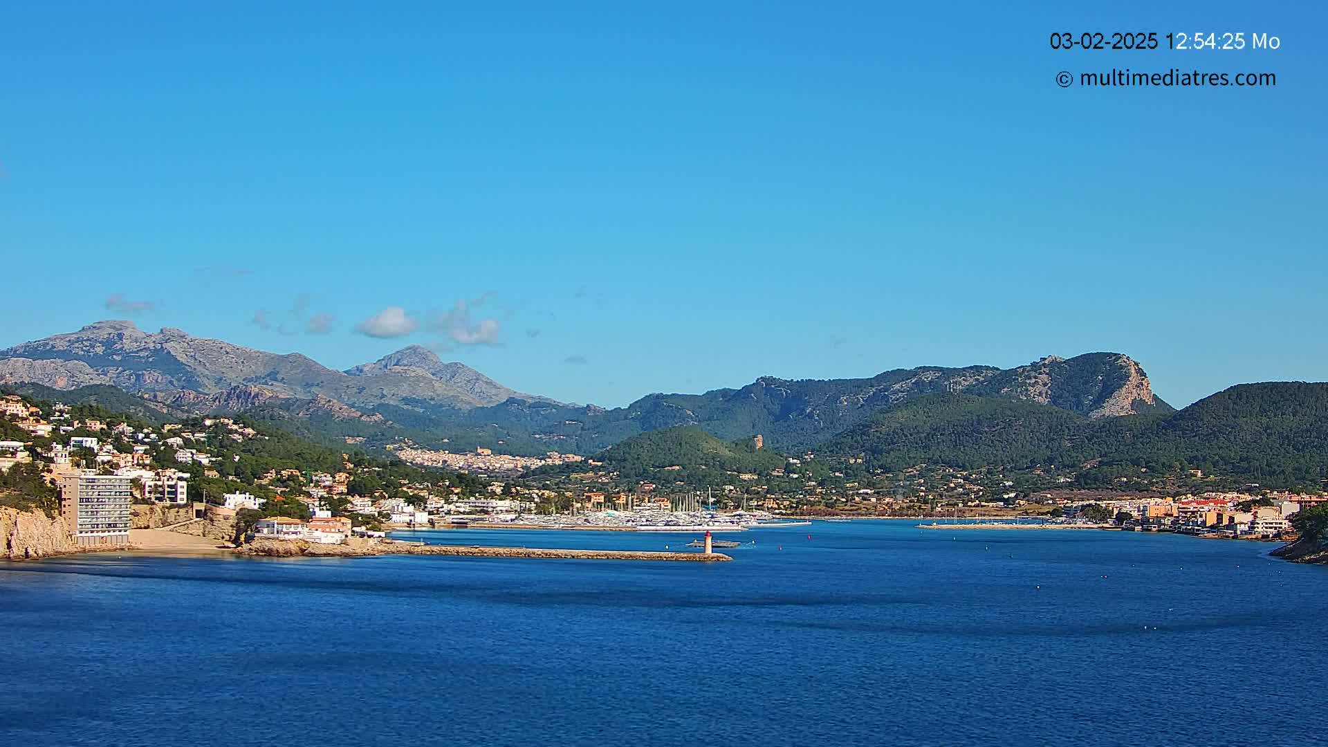A coastal town nestled between mountains and a calm blue sea under a clear blue sky.