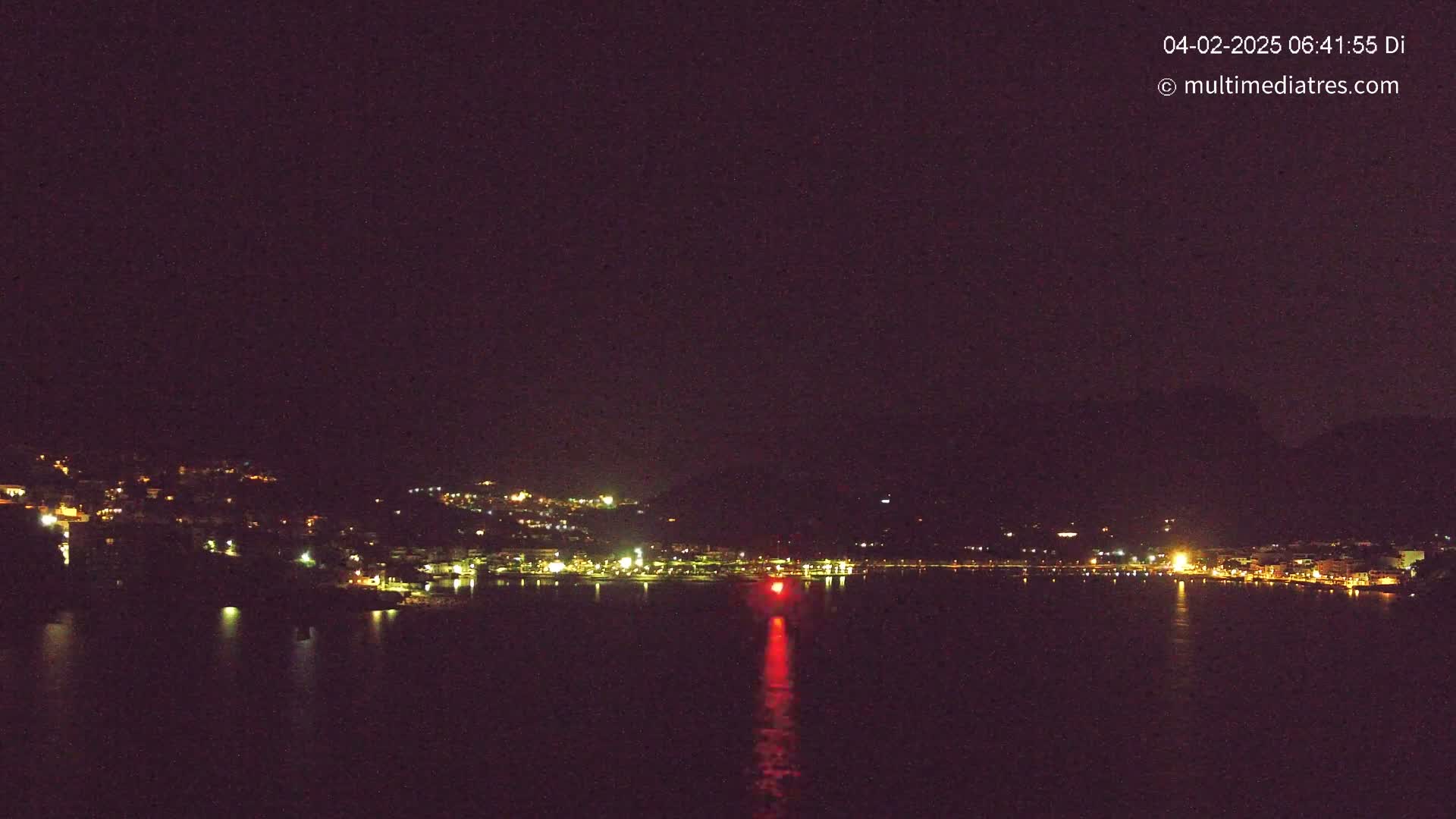 A nighttime view of a city's lights along a dark body of water under a clear, dark sky.