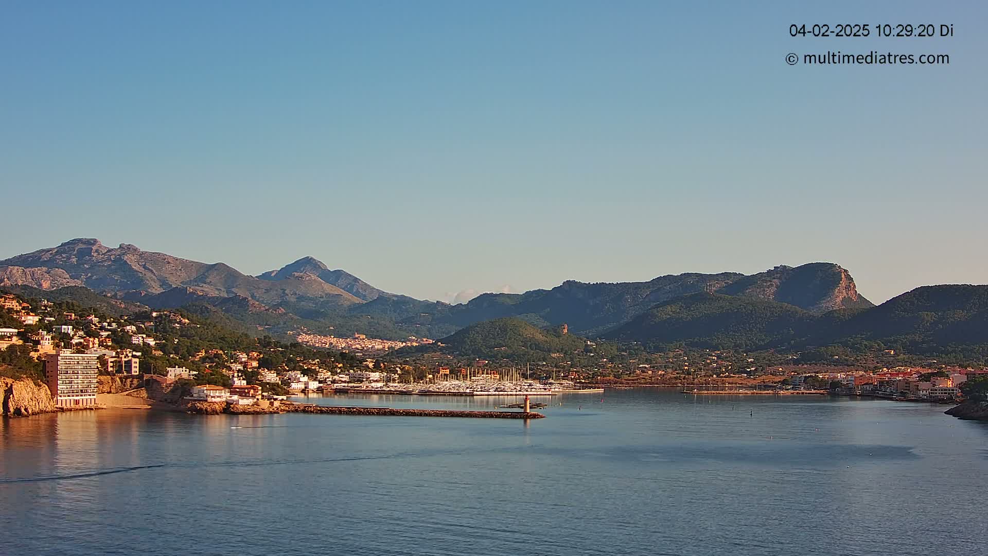 A coastal town nestled between mountains and a calm bay under a clear blue sky.