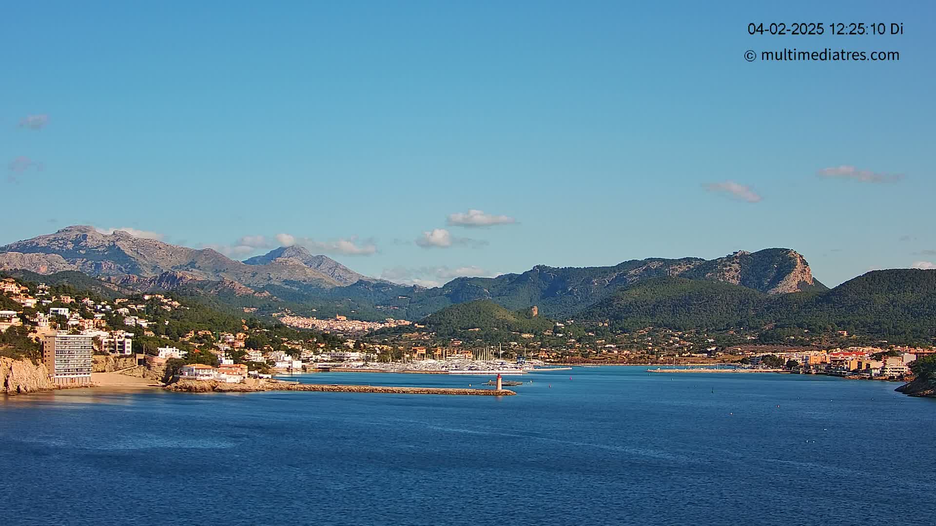 A coastal town nestled between mountains and a calm blue sea under a clear, sunny sky.
