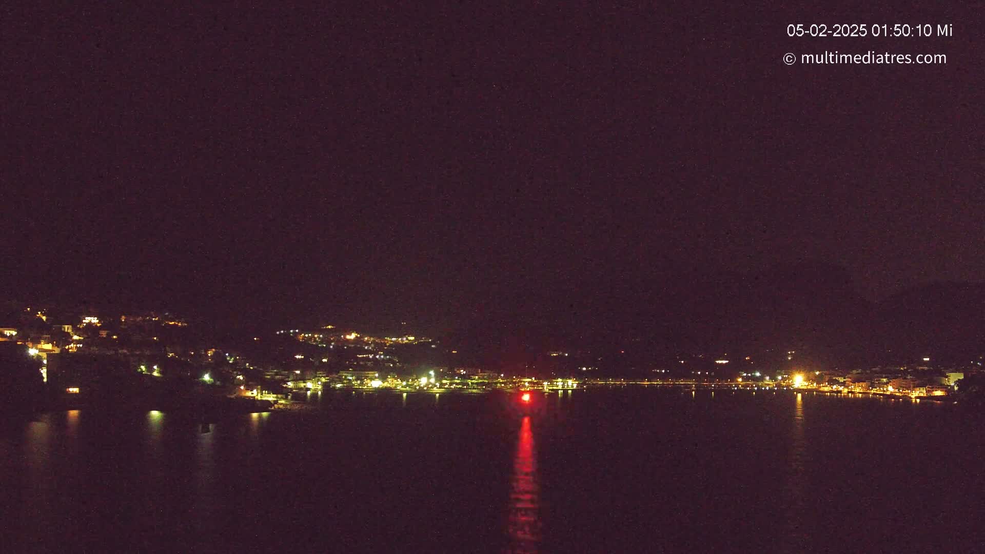 A nighttime view of a town's lights across a dark body of water under a clear, starless sky.