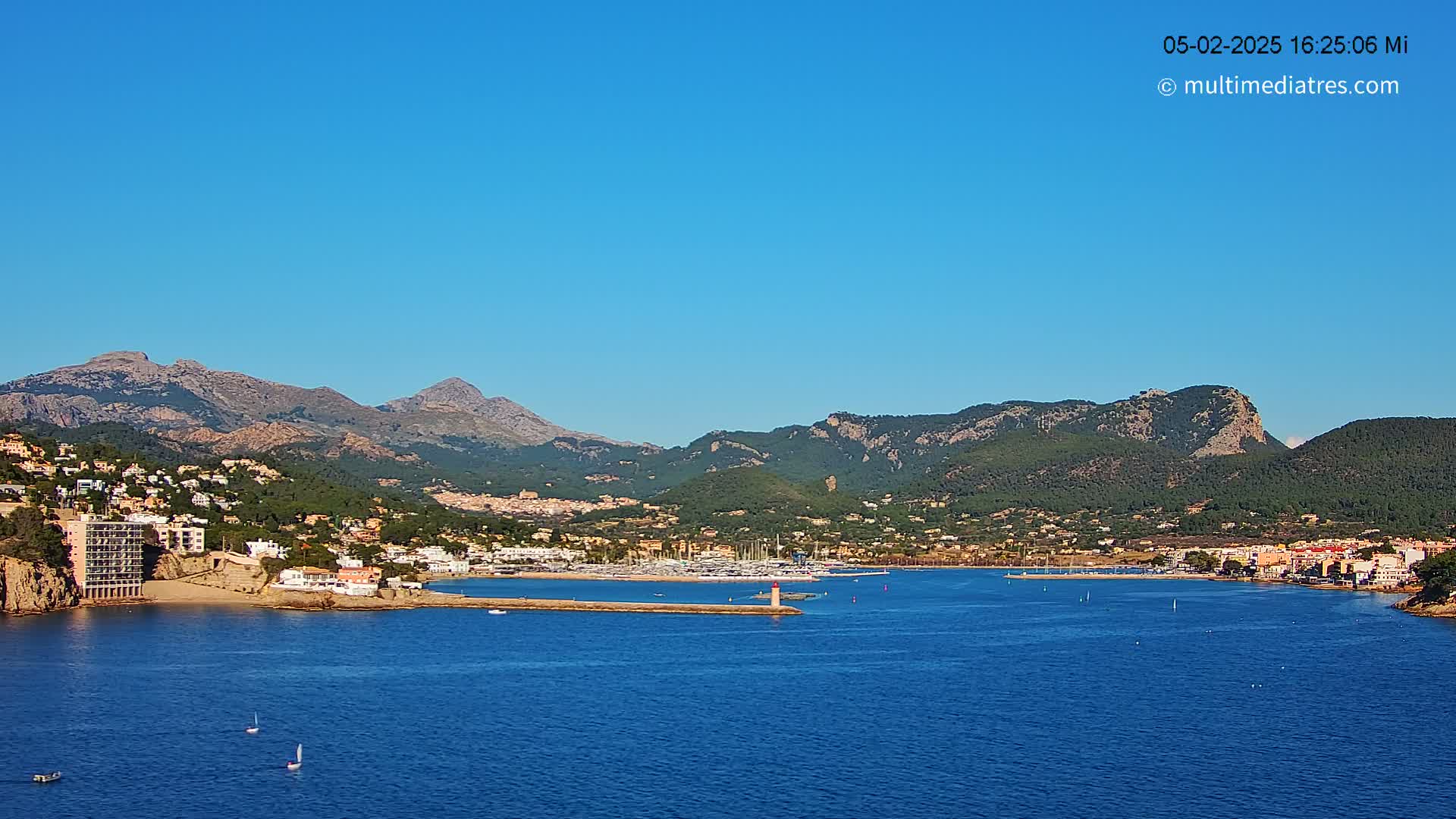 A coastal town nestled between mountains and a calm blue sea under a clear blue sky.