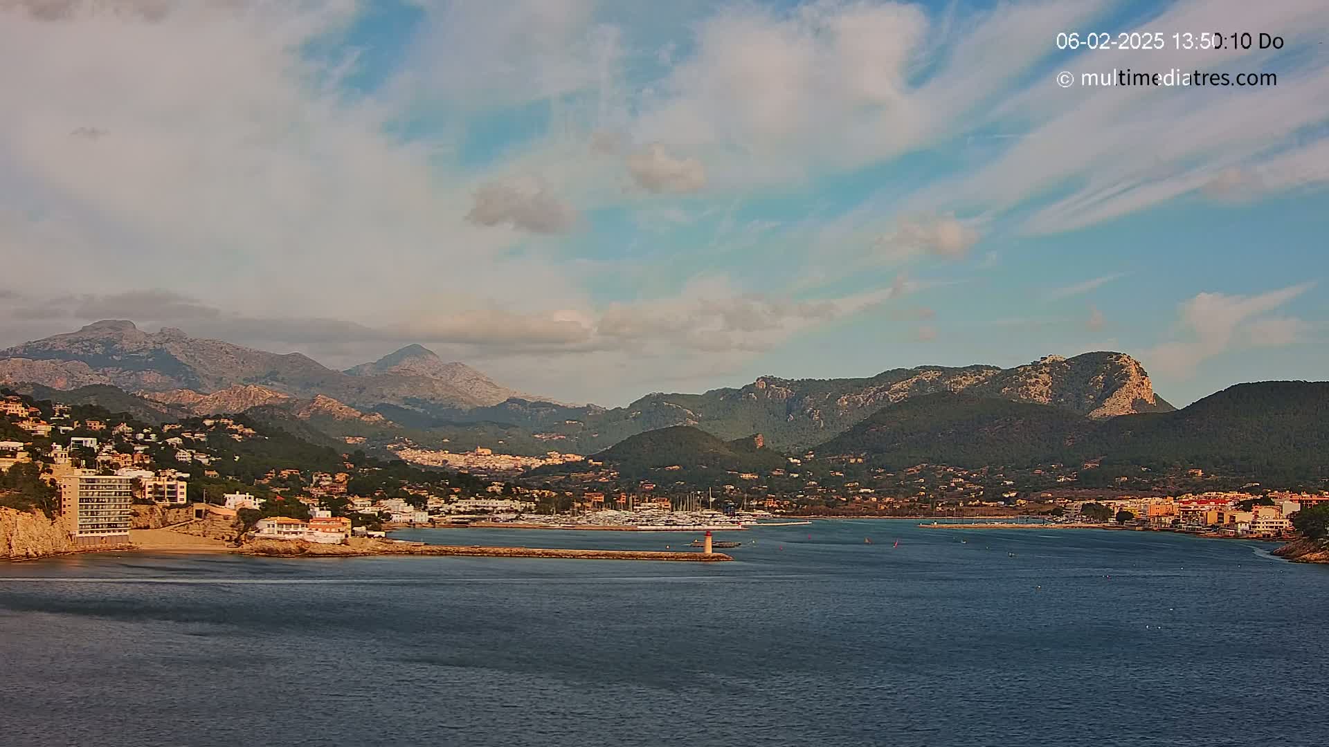 A coastal town nestled between mountains and a calm bay under a partly cloudy sky.