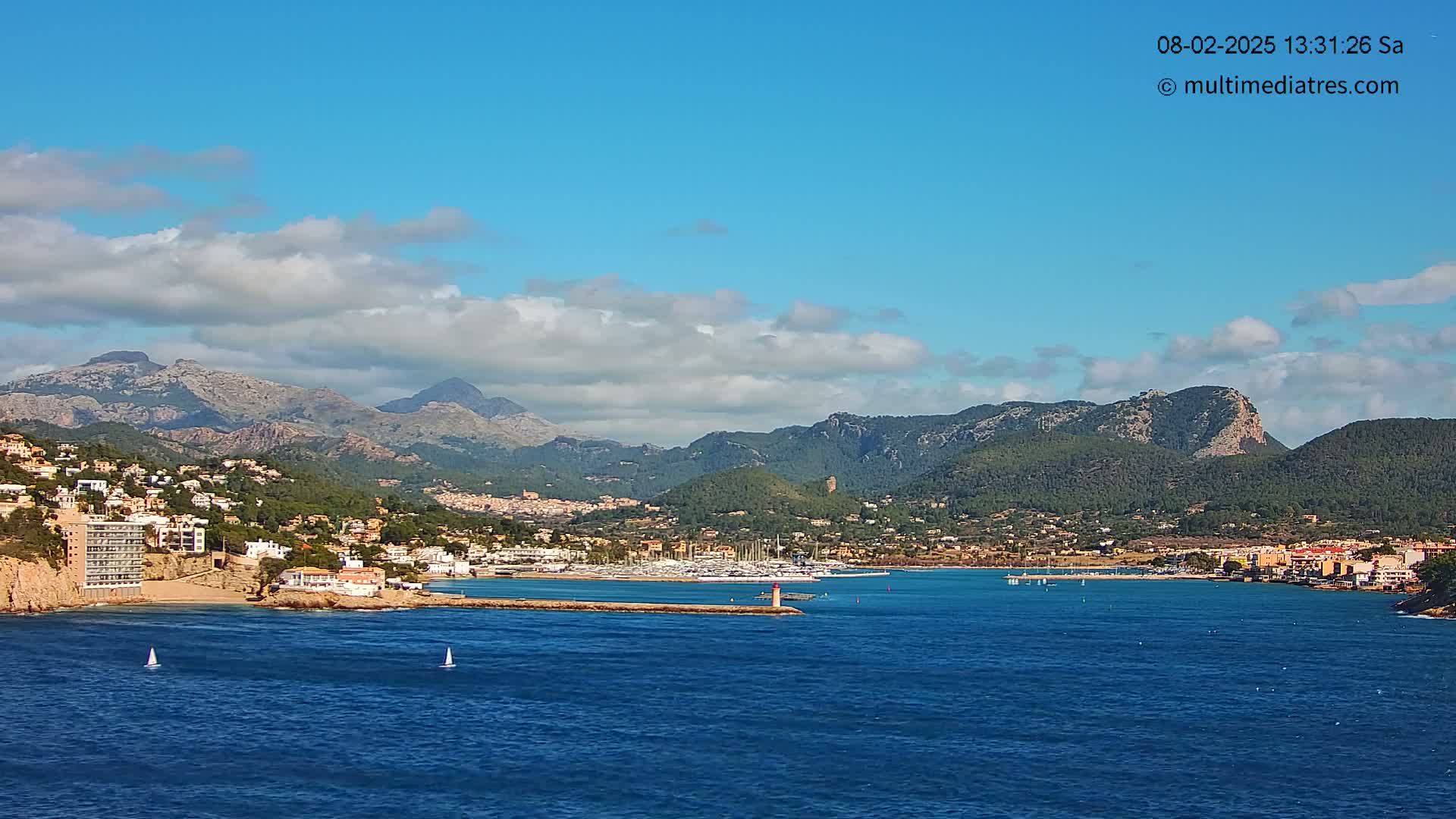 A coastal town nestled between mountains and a calm blue sea under a partly cloudy sky.