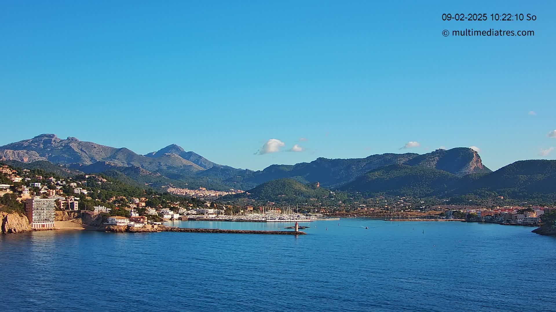 A coastal town nestled between mountains and a calm blue sea under a clear blue sky.
