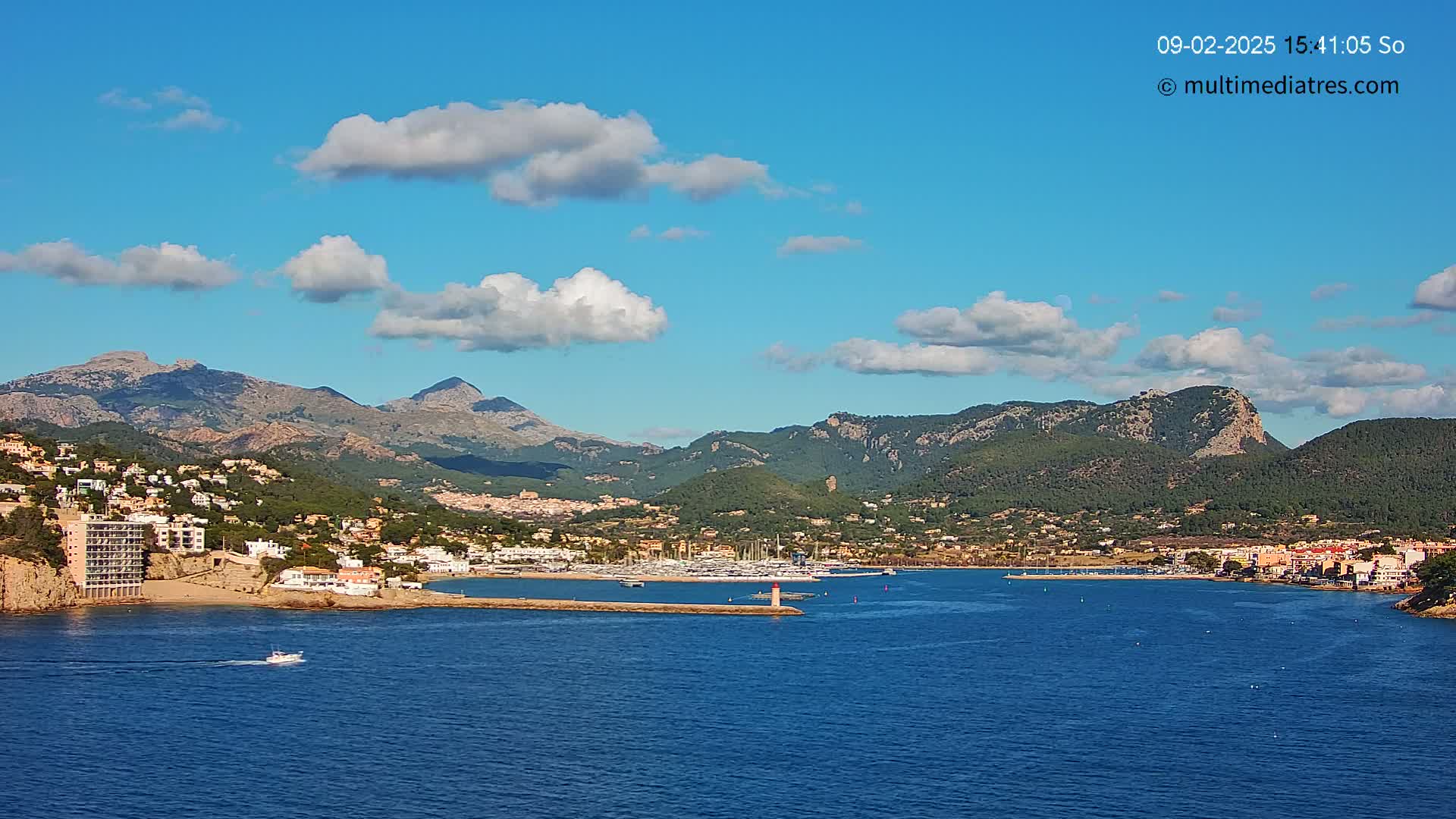 A coastal town nestled between mountains and a calm blue sea under a partly cloudy sky.