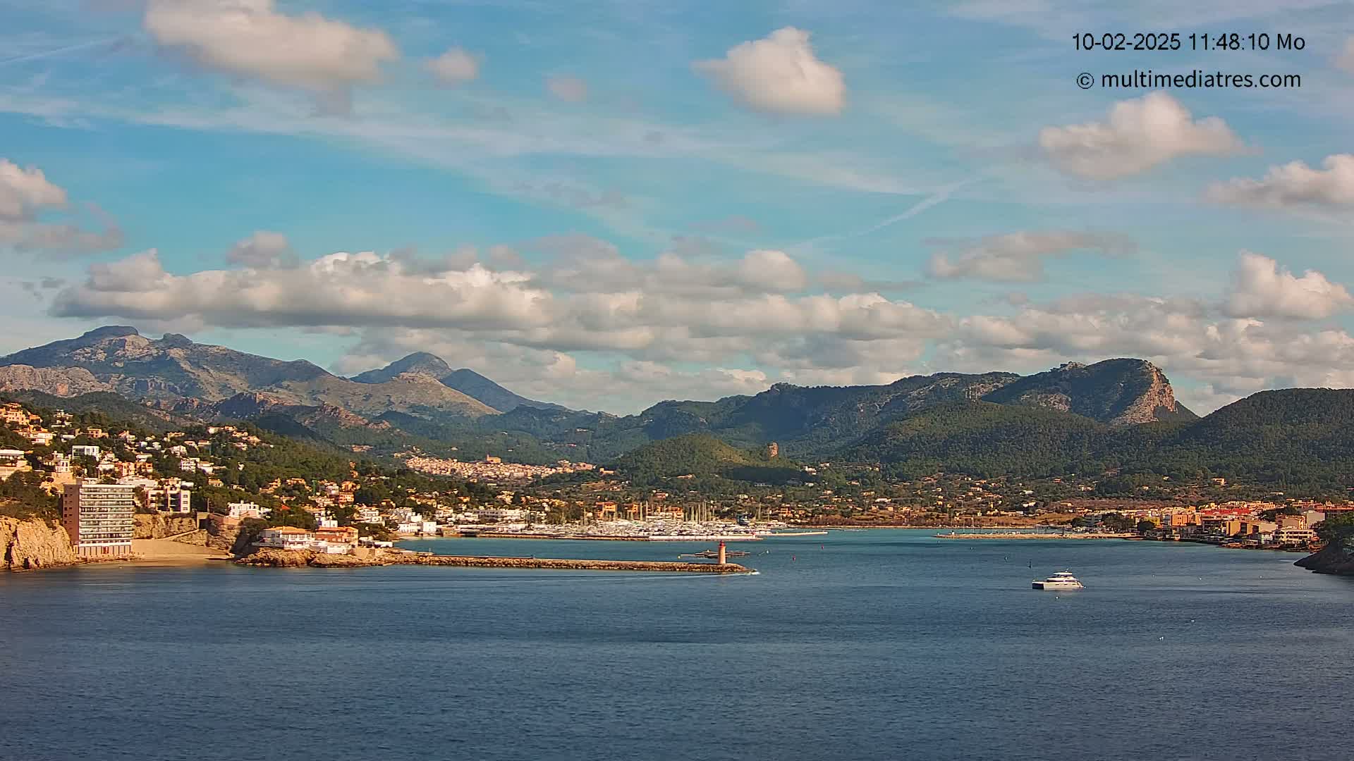 A coastal town nestled between mountains and a calm bay under a partly cloudy sky.