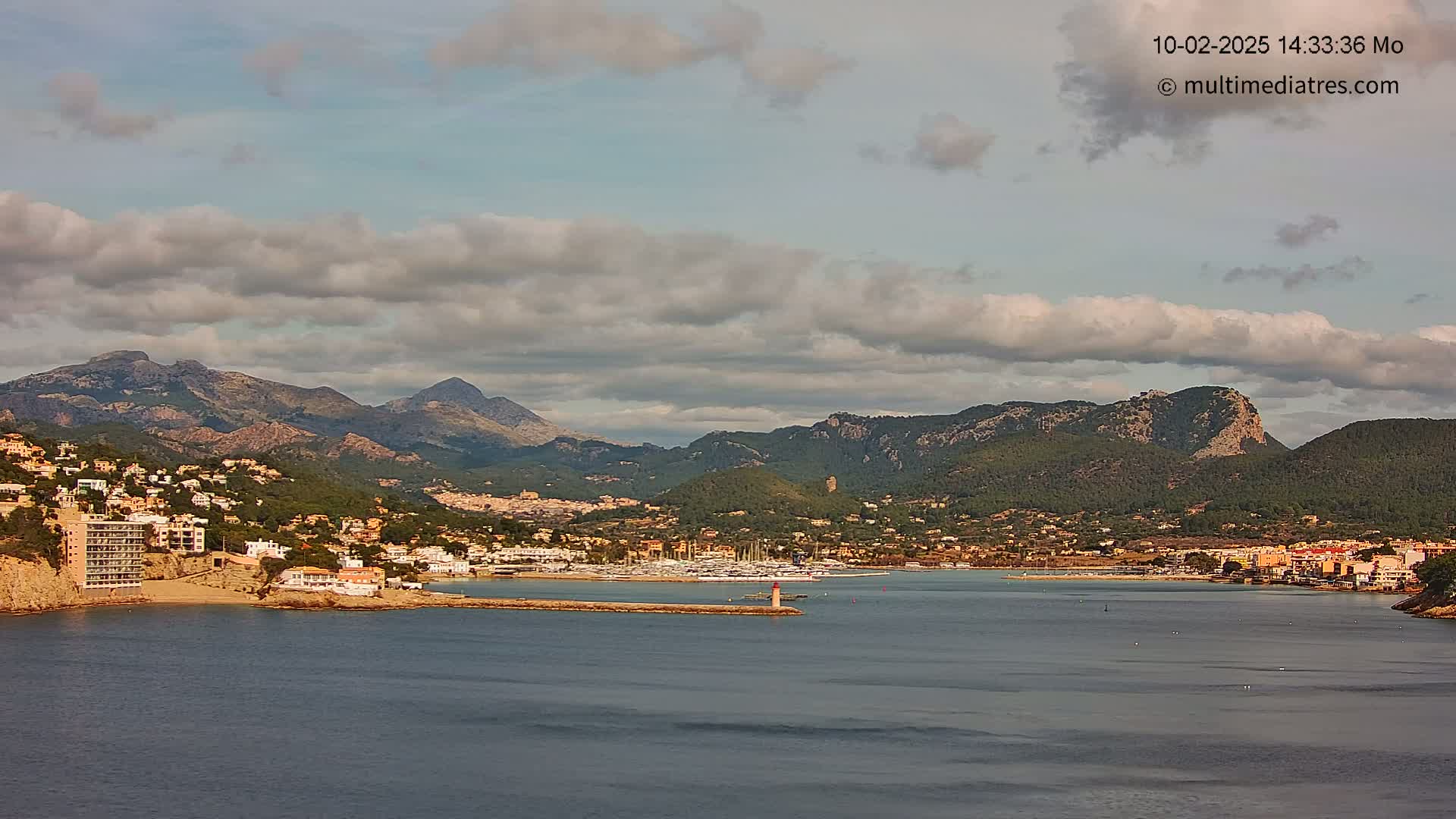 A coastal town nestled between mountains and a calm bay under a partly cloudy sky.