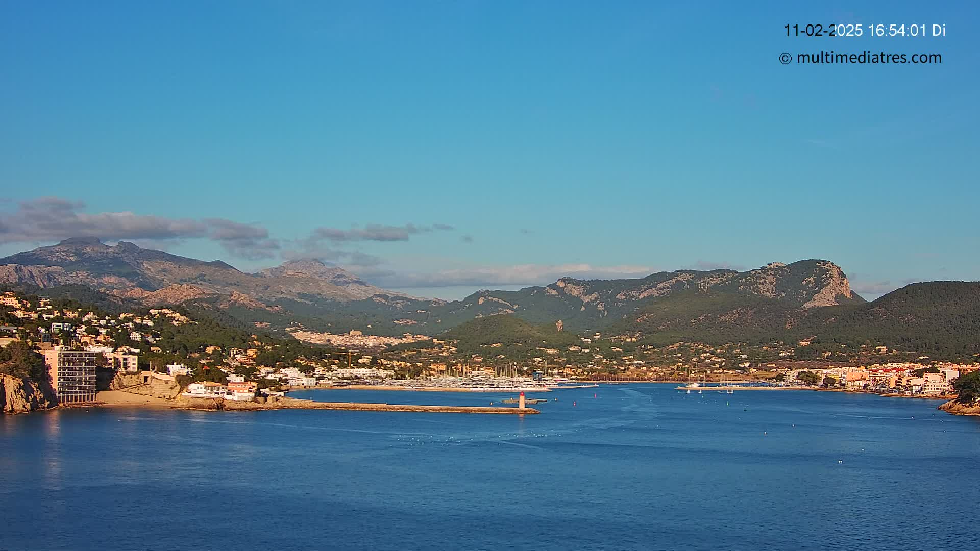 A coastal town nestled between mountains and a calm blue sea under a clear blue sky.