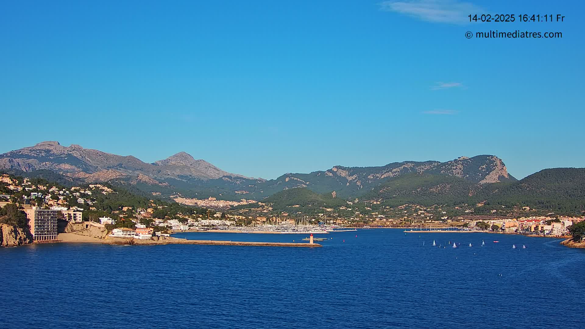 A coastal town nestled between mountains and a calm blue sea under a clear, sunny sky.