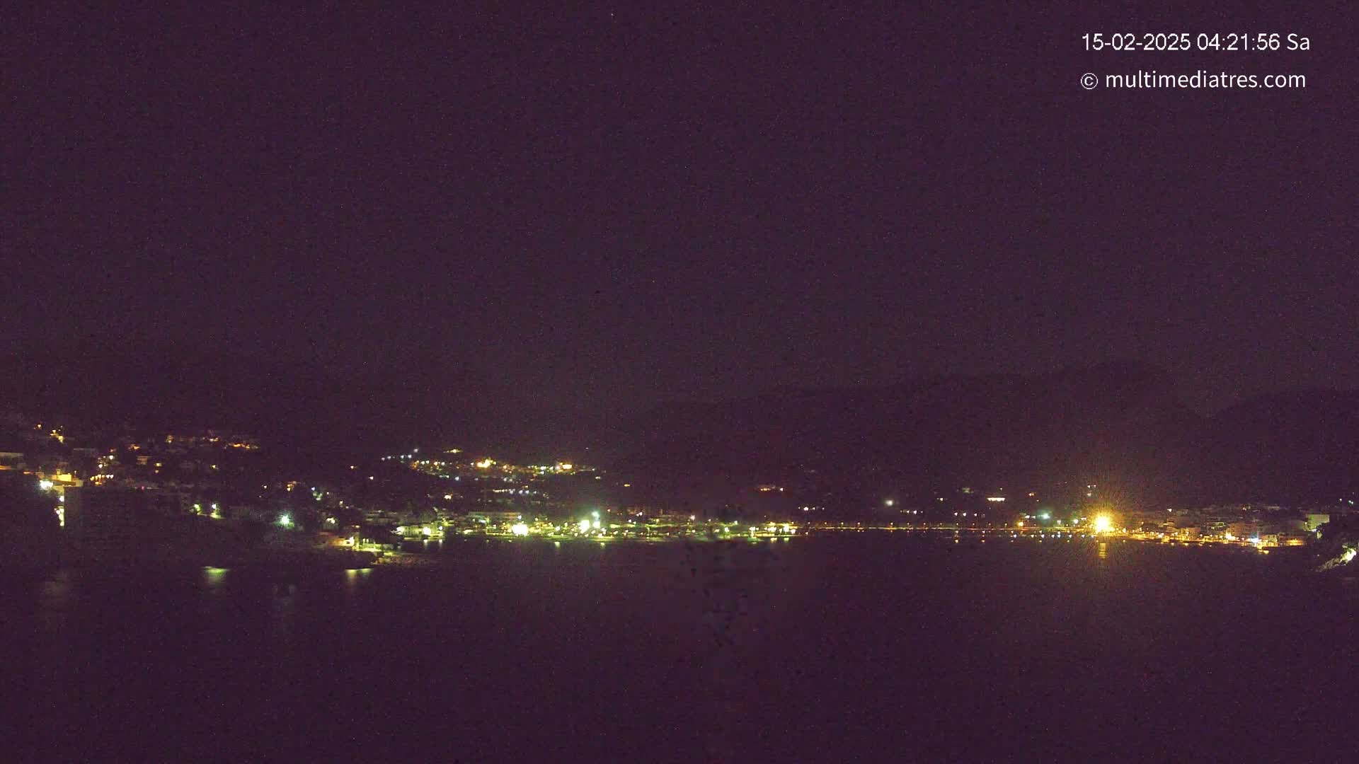 A nighttime view of a coastal town with its lights illuminated against a dark sky.