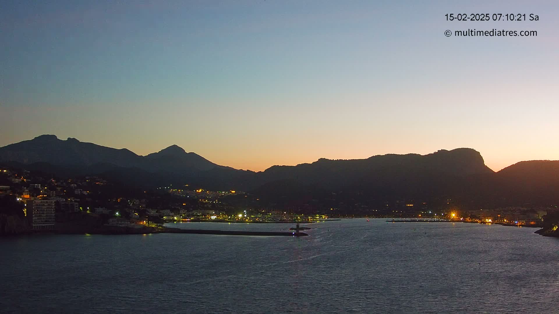 A coastal town with lights illuminated against a dark mountain range at twilight.
