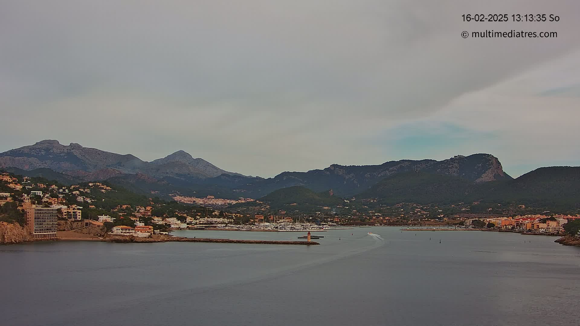A coastal town nestled between mountains, with a calm harbor and overcast skies.