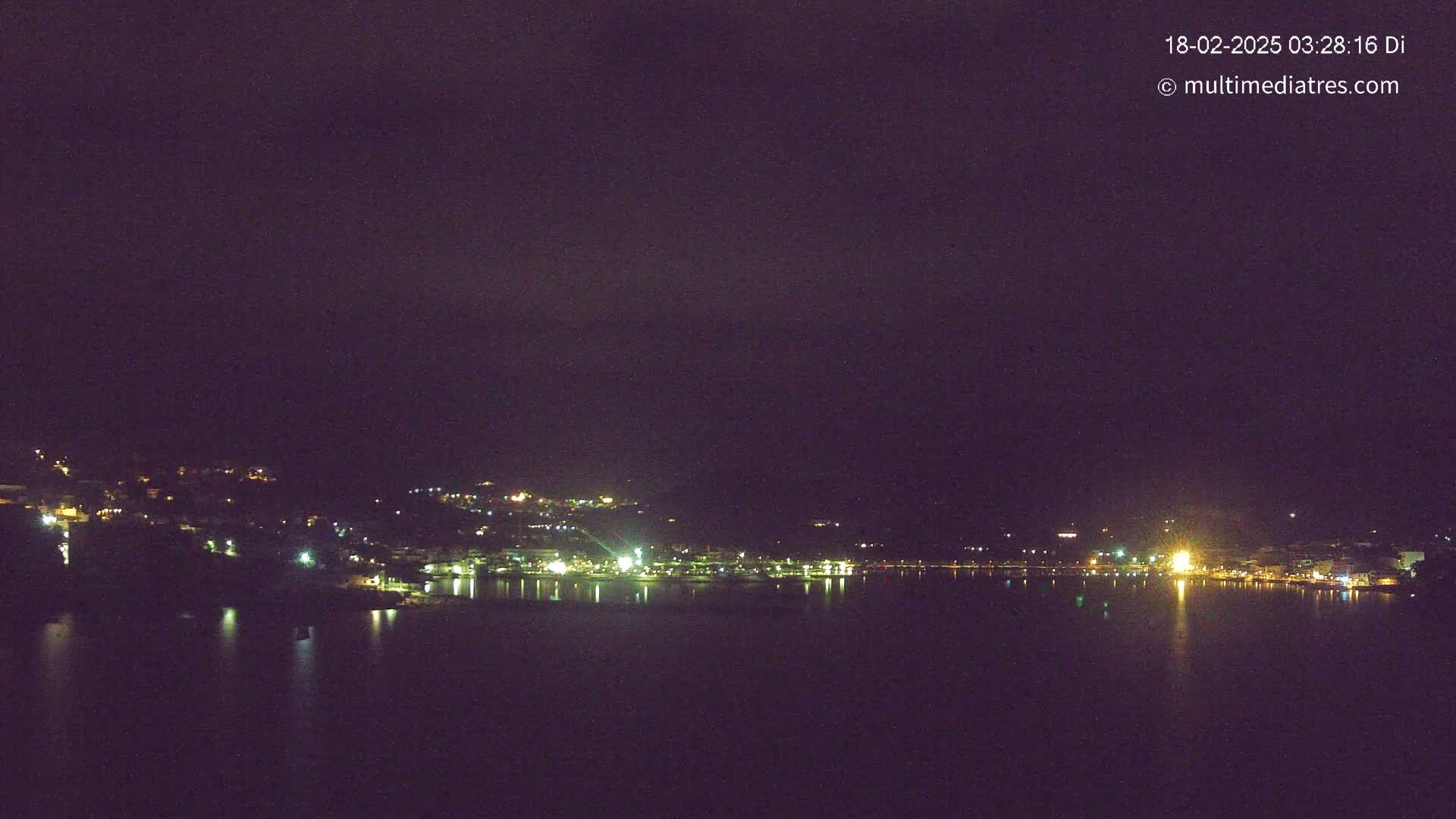 A nighttime view of a town's lights across a dark body of water under a clear, dark sky.