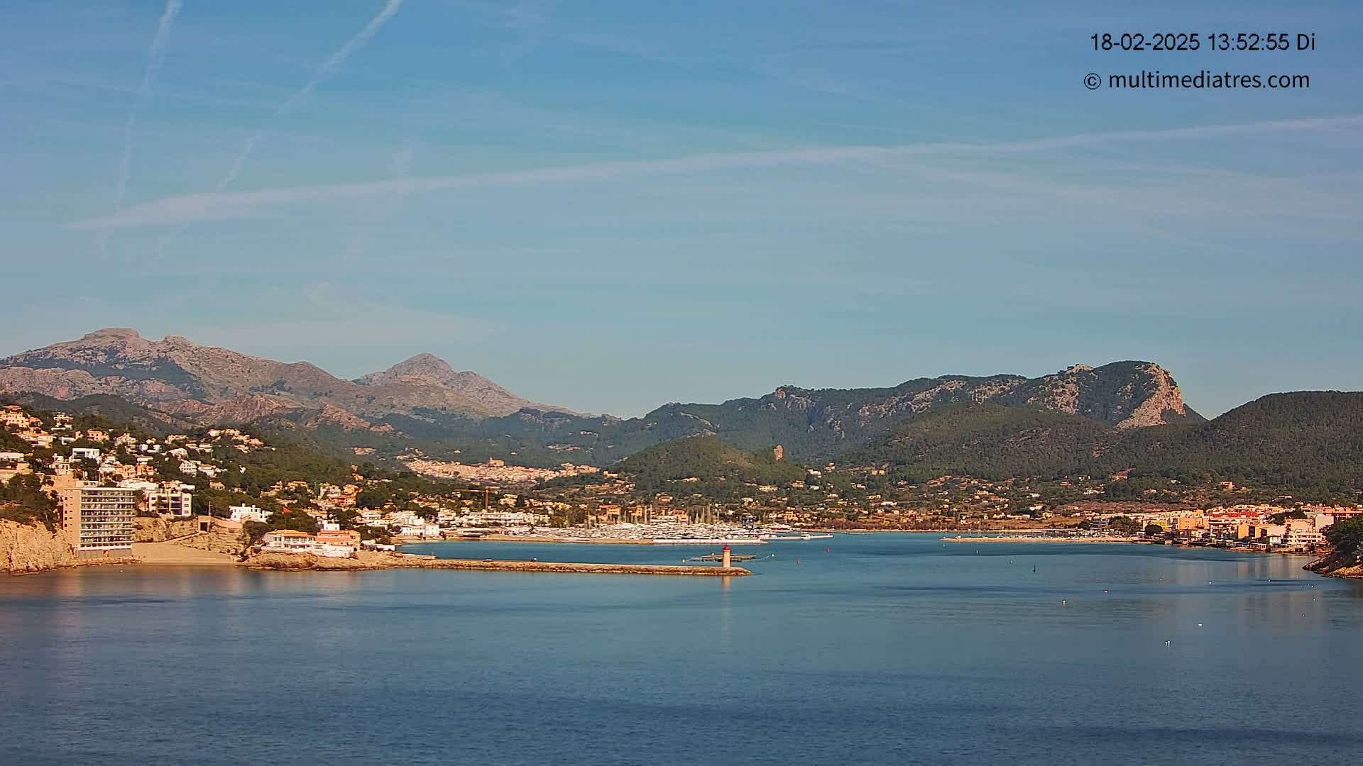 A clear, sunny day reveals a coastal town nestled between mountains and a calm bay filled with boats.