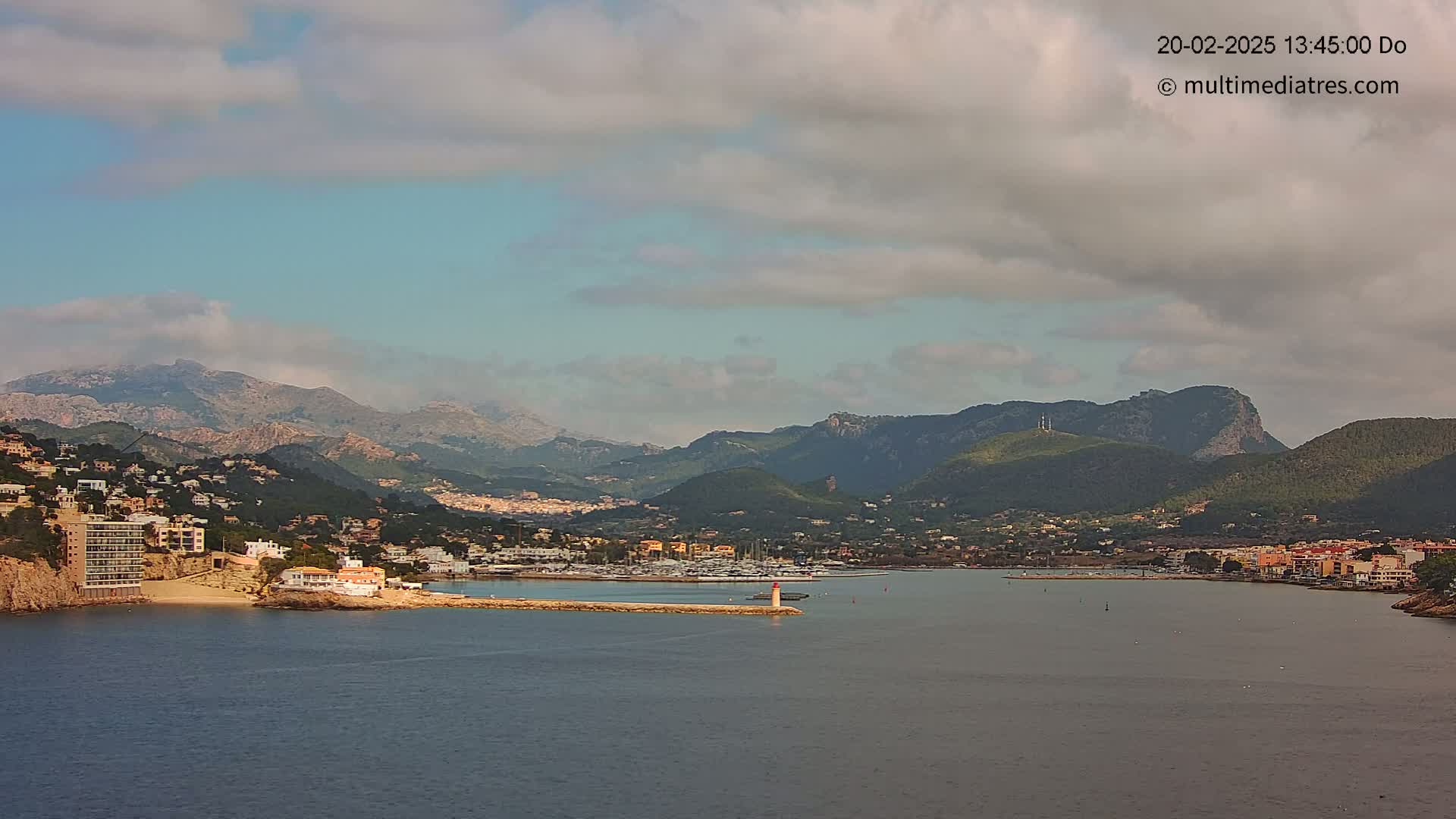 A coastal town nestled between mountains and a calm body of water under a partly cloudy sky.