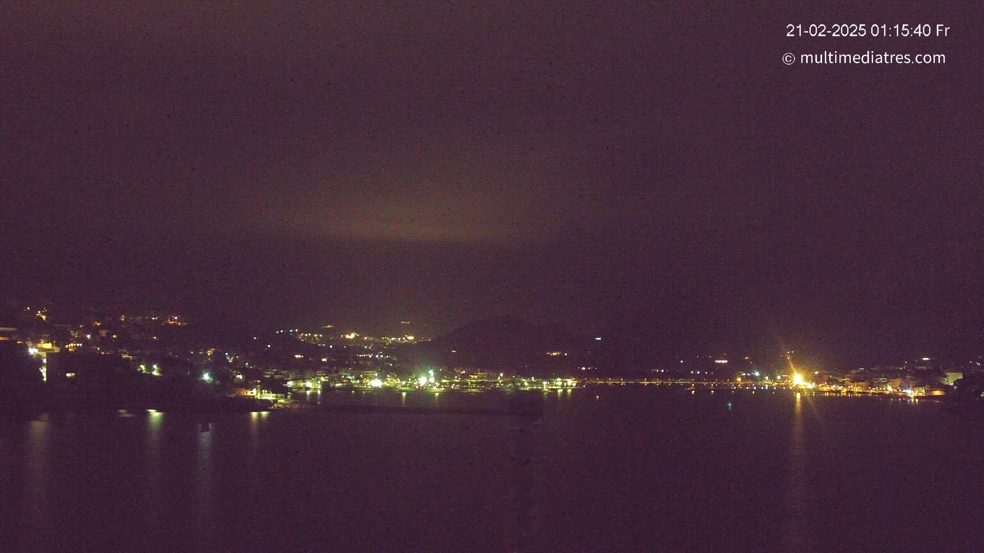 A nighttime view of a city's lights along a dark, calm body of water under a dusky sky.