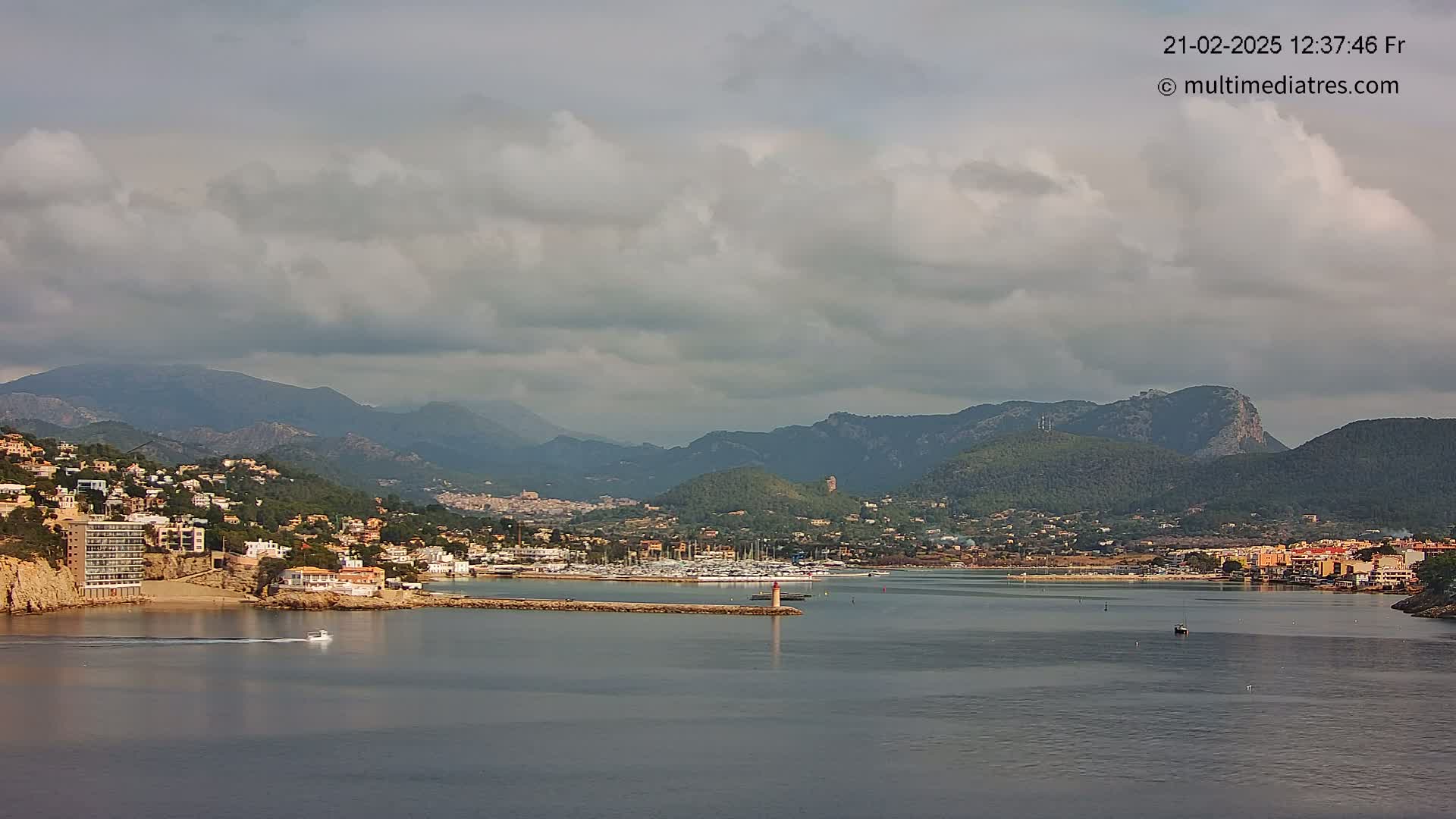 A coastal town nestled in a bay, surrounded by mountains under a cloudy sky.