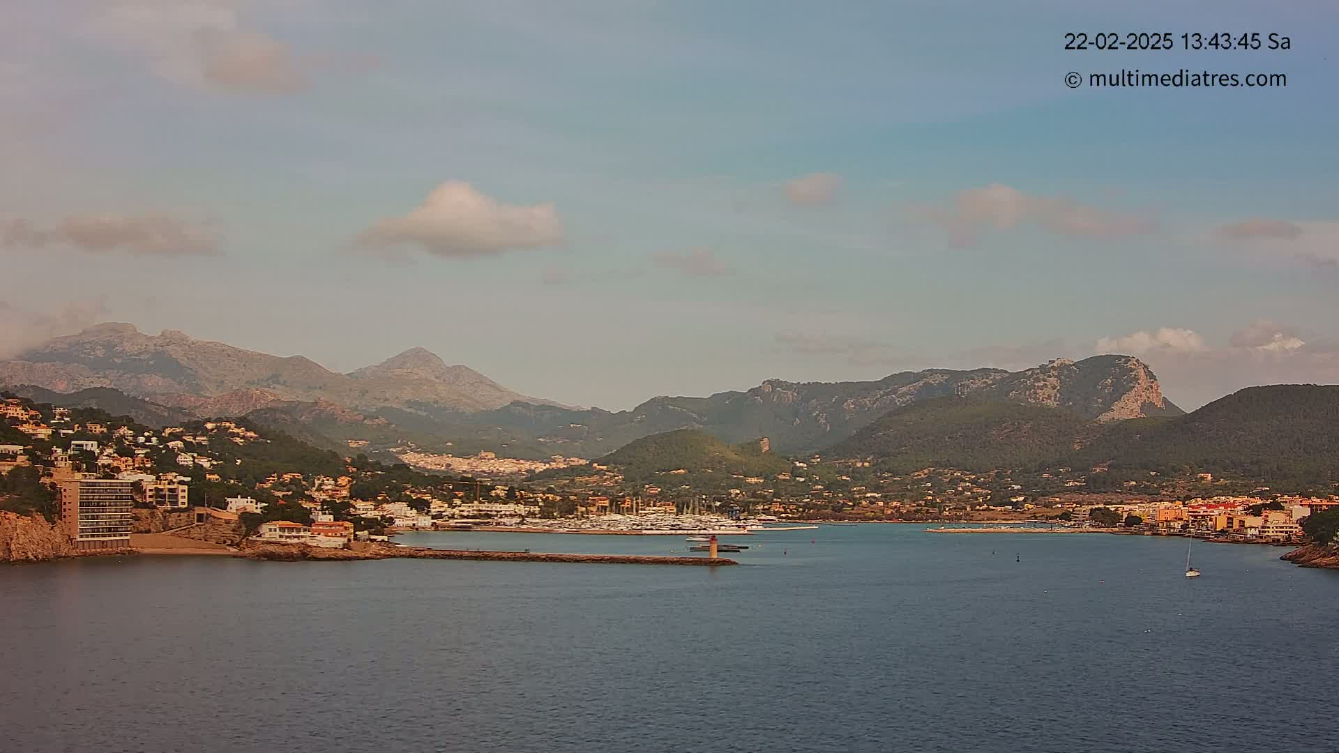 A coastal town nestled among mountains, with a calm bay filled with boats under a mostly clear sky.