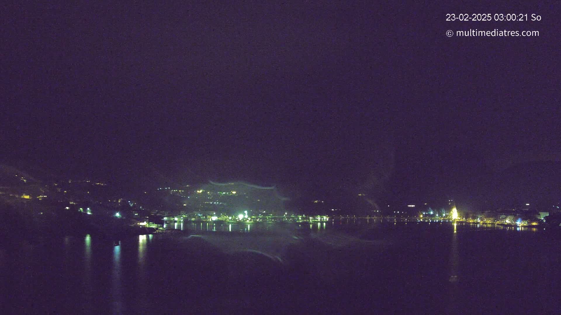 A nighttime view of a city skyline across a calm body of water under a dark, clear sky.