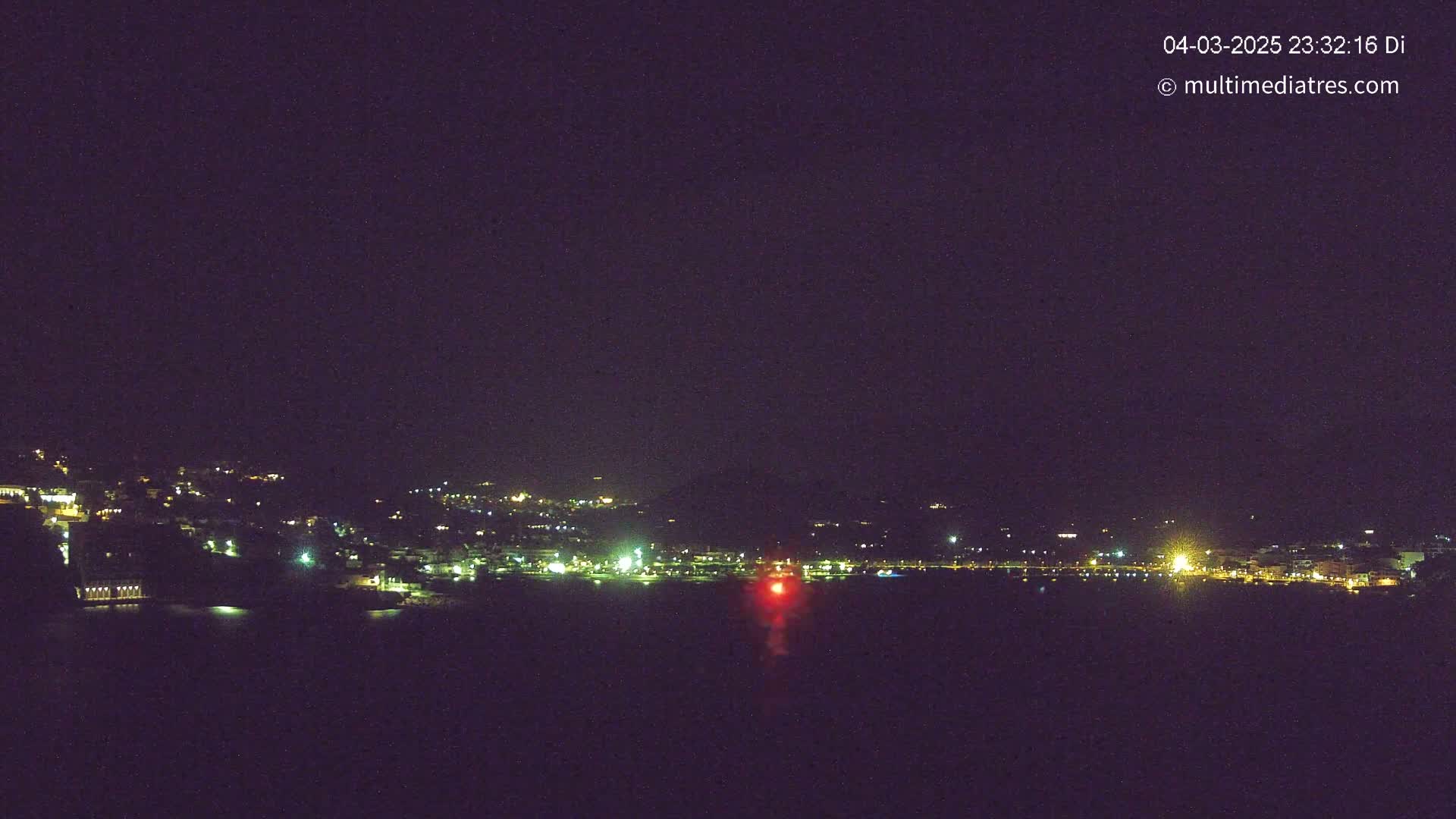 A nighttime view of a coastal town with its lights illuminated across a dark body of water under a clear night sky.