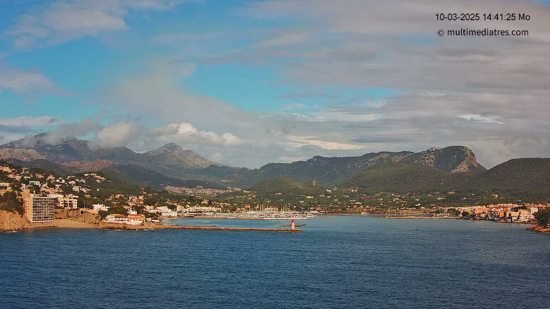 A coastal town nestled between mountains and a calm sea under a partly cloudy sky.