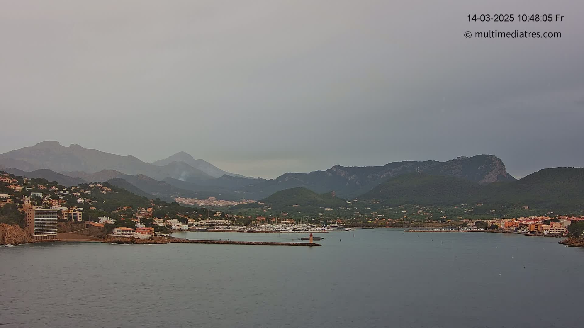 A coastal town nestled between mountains and a calm sea under an overcast sky.